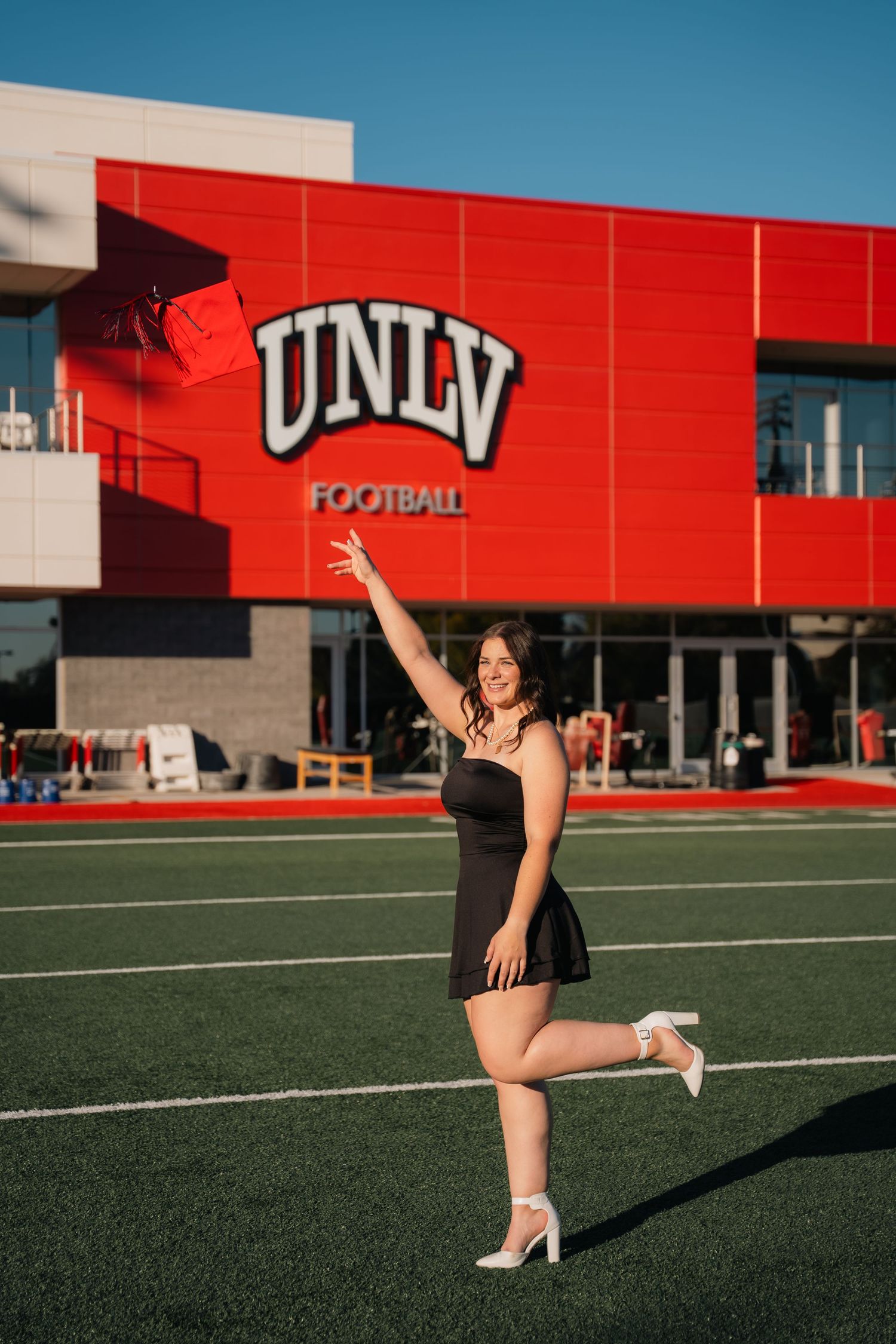 Graduation photo session on UNLV football field with red building in background.