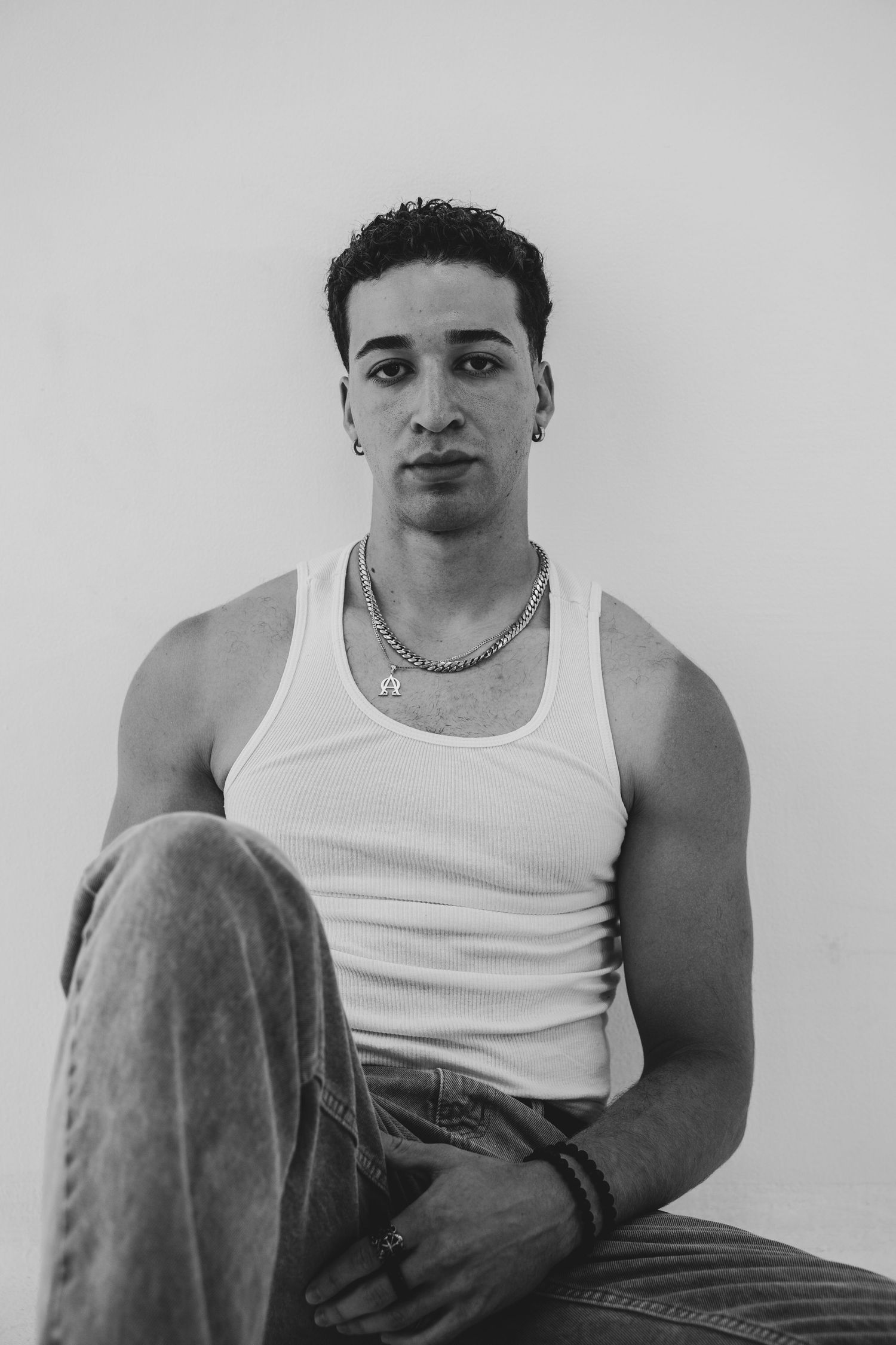Person in white tank top seated against wall in contemplative black and white portrait series.