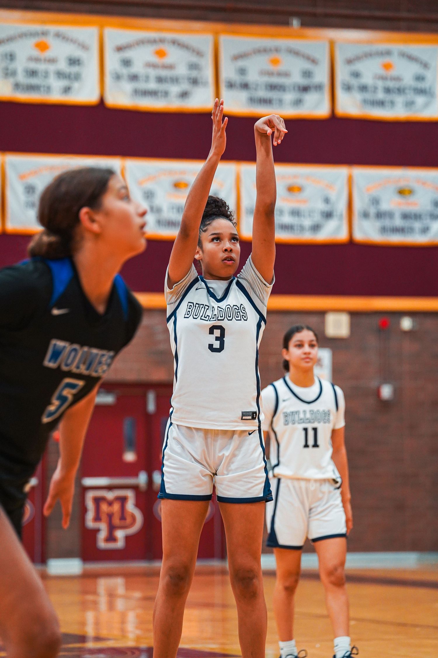 Basketball player shoots free throw while teammates watch in high school gym.