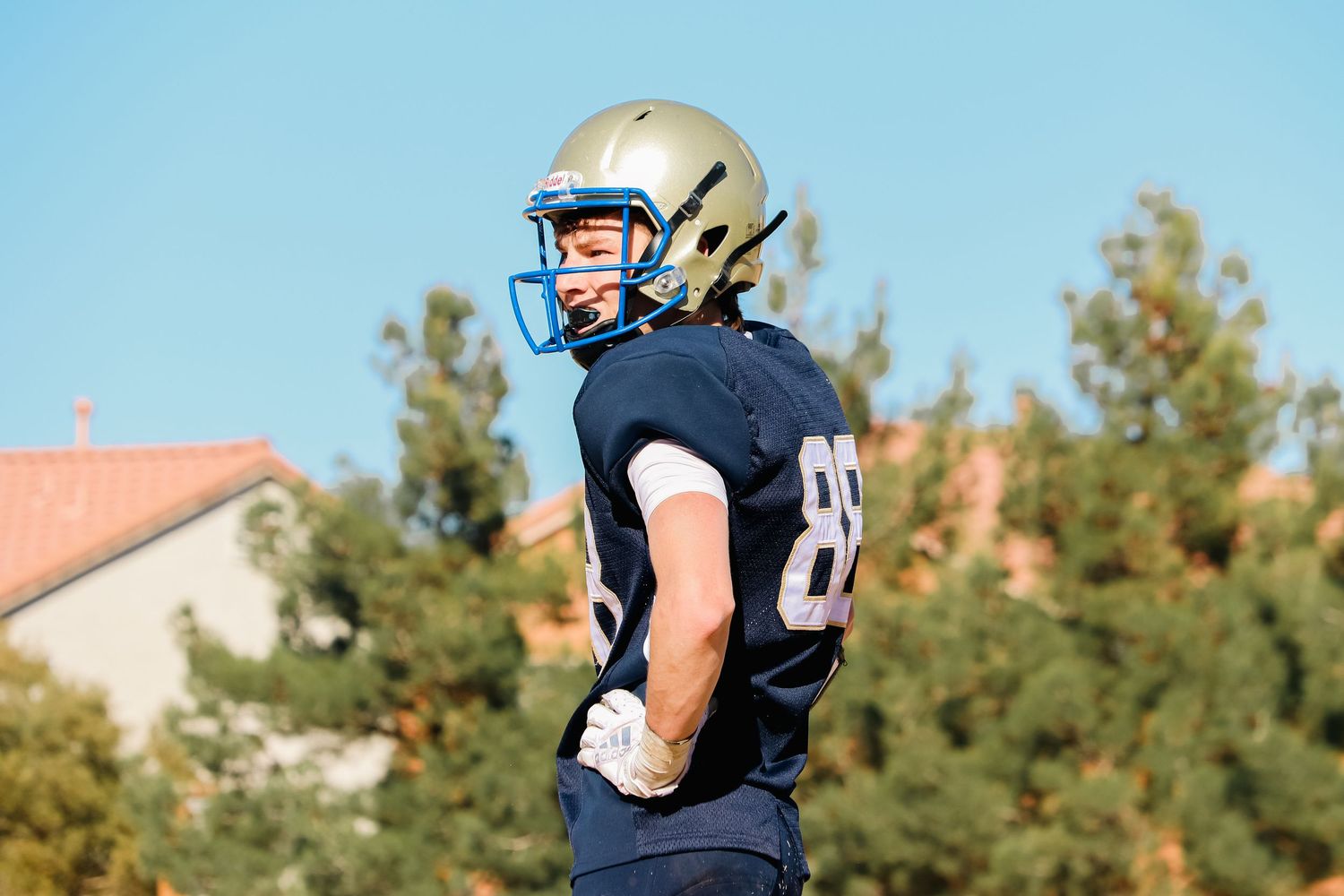 Football player in navy uniform with number 85 standing on field with trees in background.