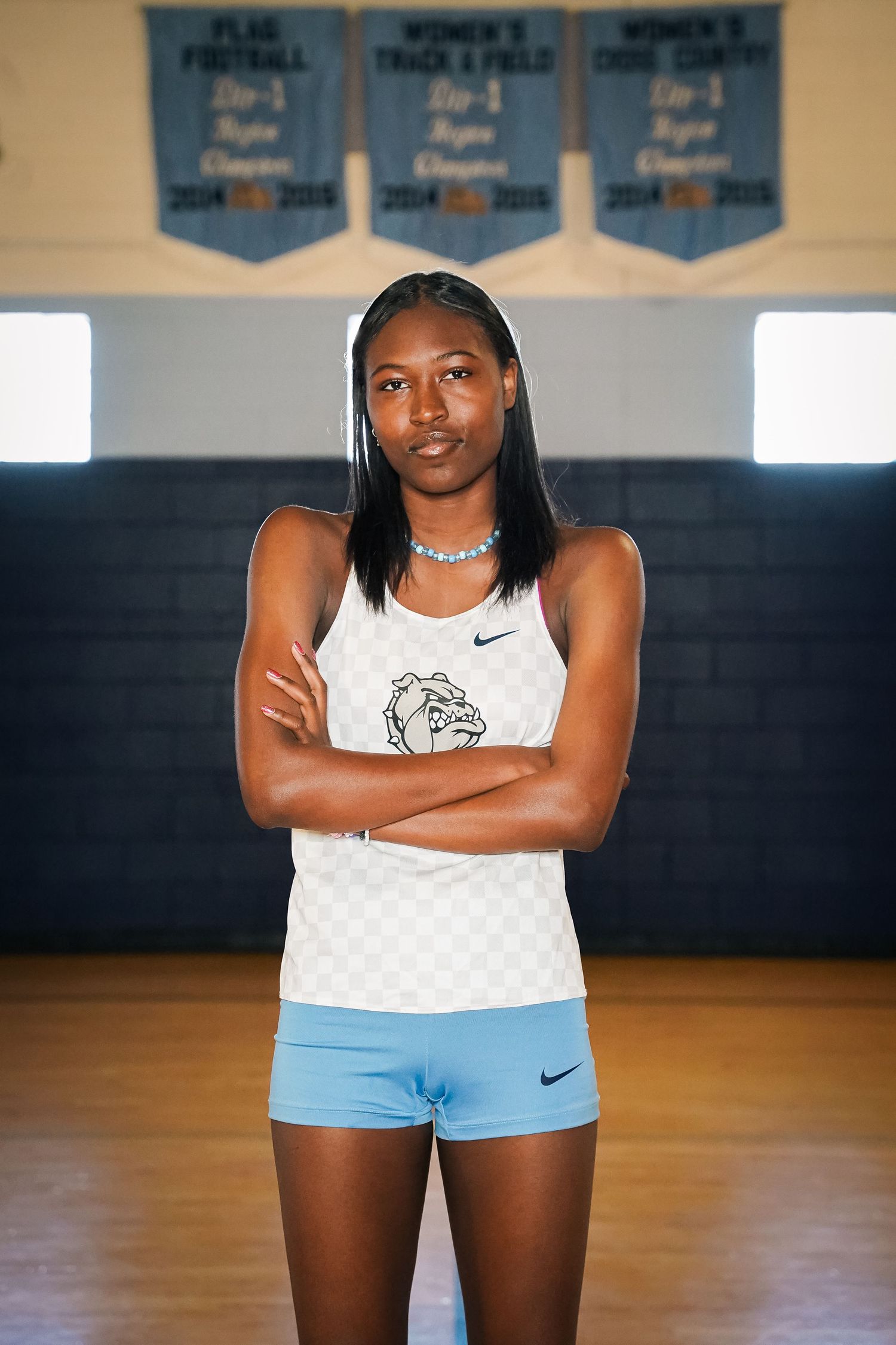 Indoor portrait of athlete in white checkered uniform standing in gymnasium with championship banners.