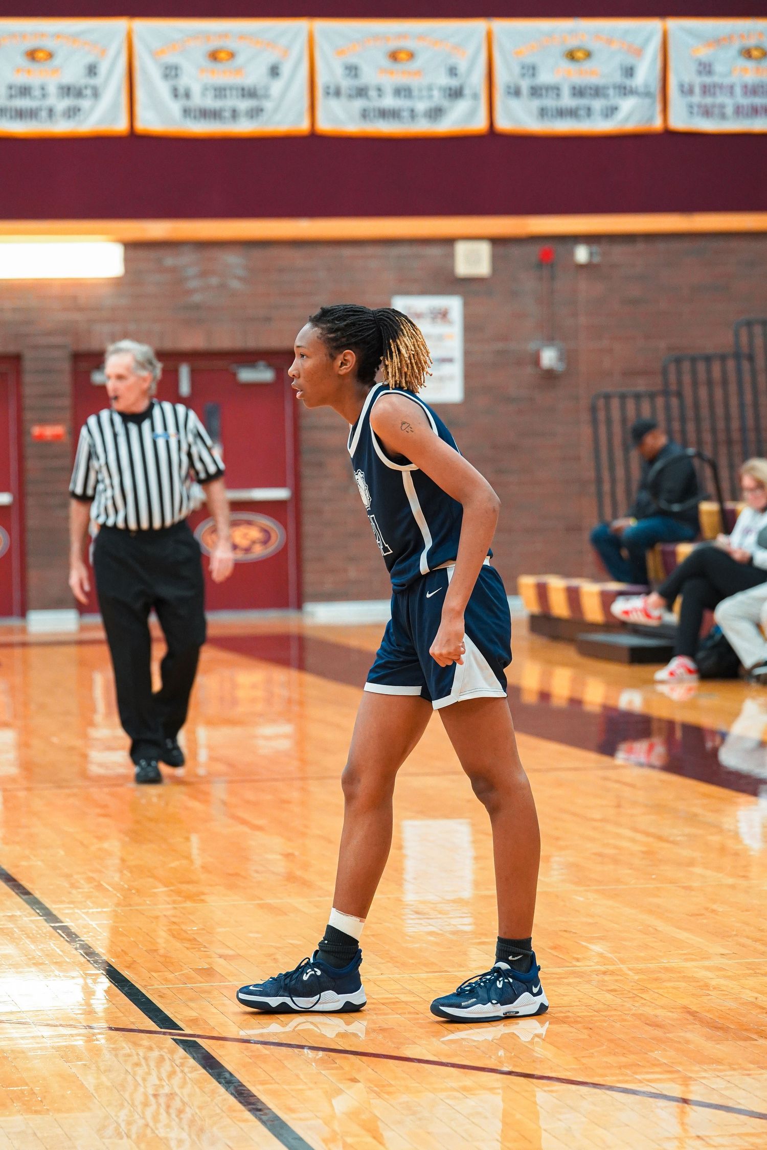 Lower body view of basketball players and referee on wooden court during game action.