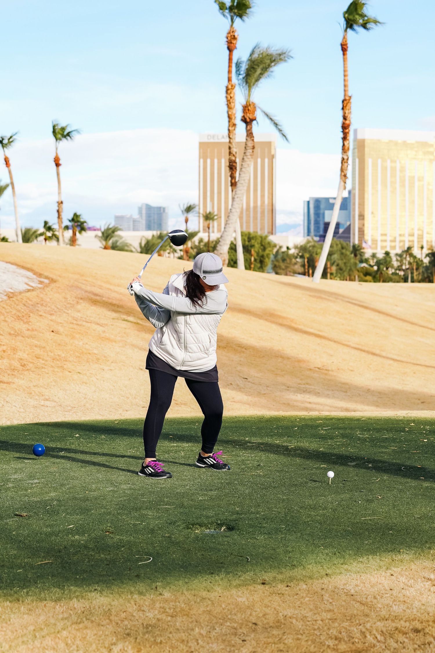 Golfer addresses ball on desert course with Mandalay Bay and palm trees in background.