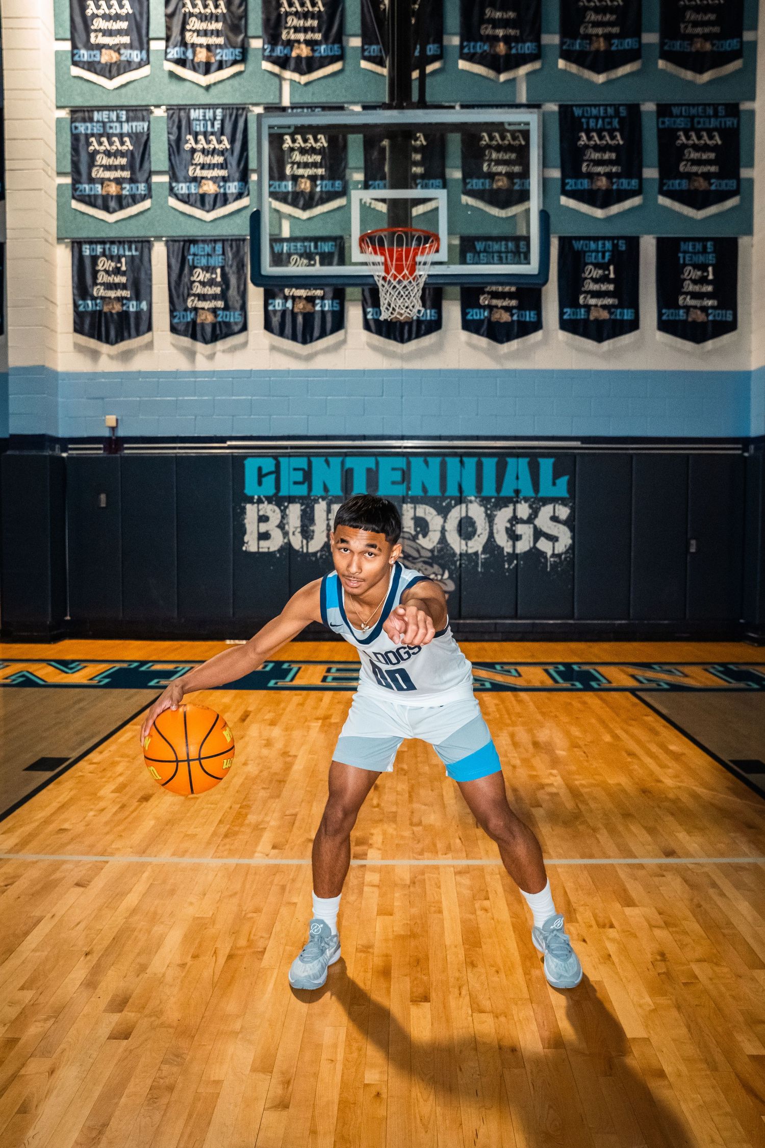 Basketball player in Centennial uniform demonstrates dribbling stance on hardwood court.
