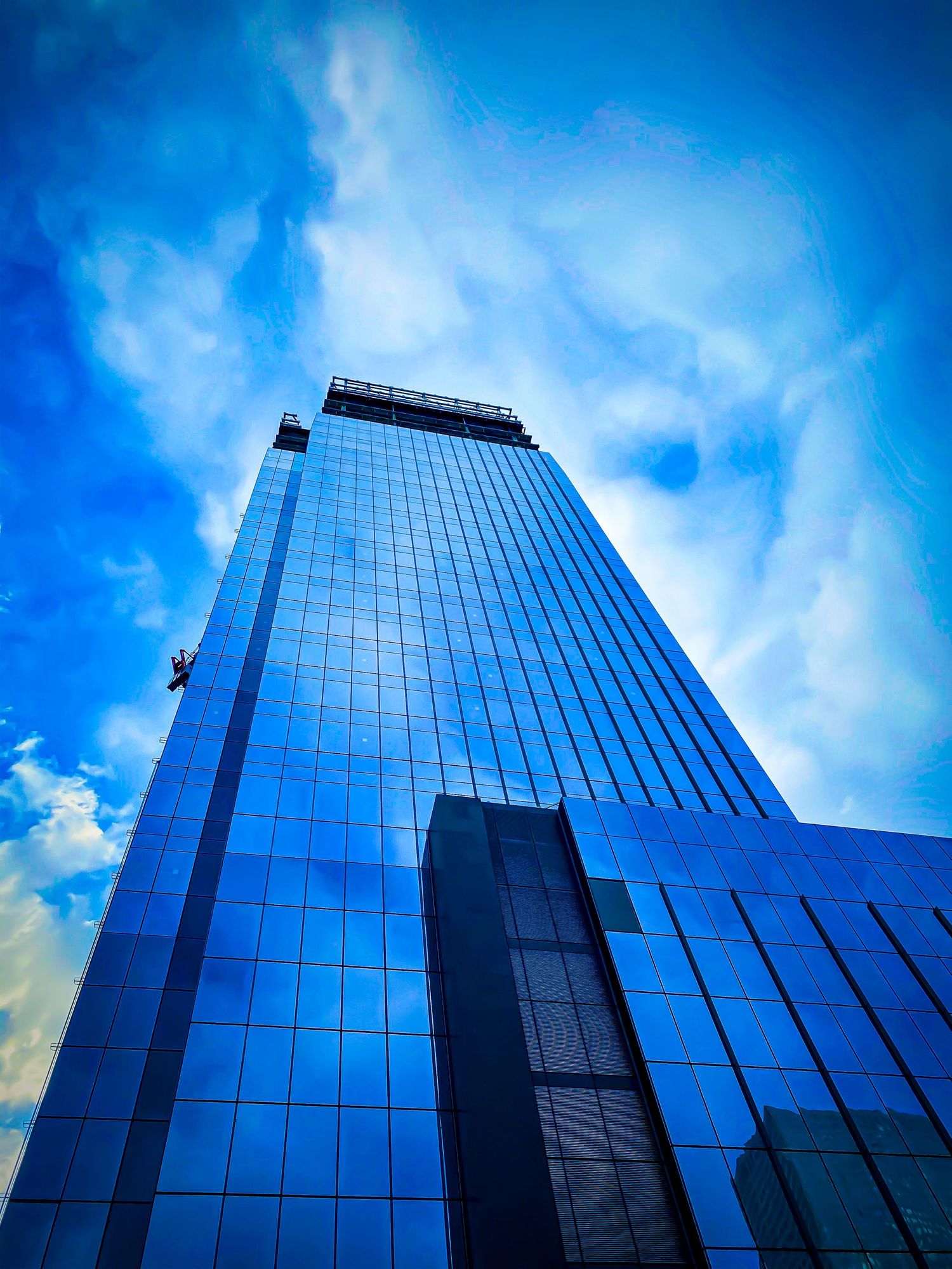 Modern glass skyscraper reaching into bright blue sky with dramatic clouds.