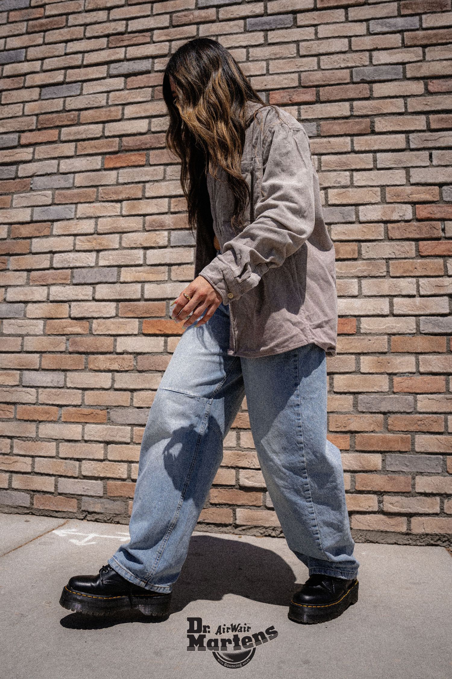 Person in loose jeans and Dr. Martens boots walking along brick wall.