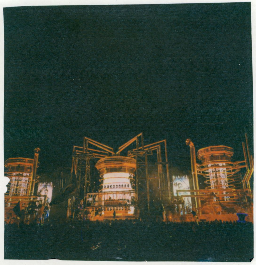 Industrial structures illuminated in orange against dark night sky in urban setting.