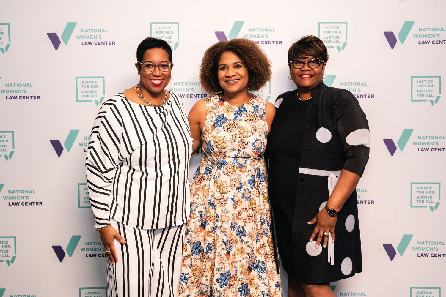 Three attendees pose for photo against branded step-and-repeat banner at formal event.