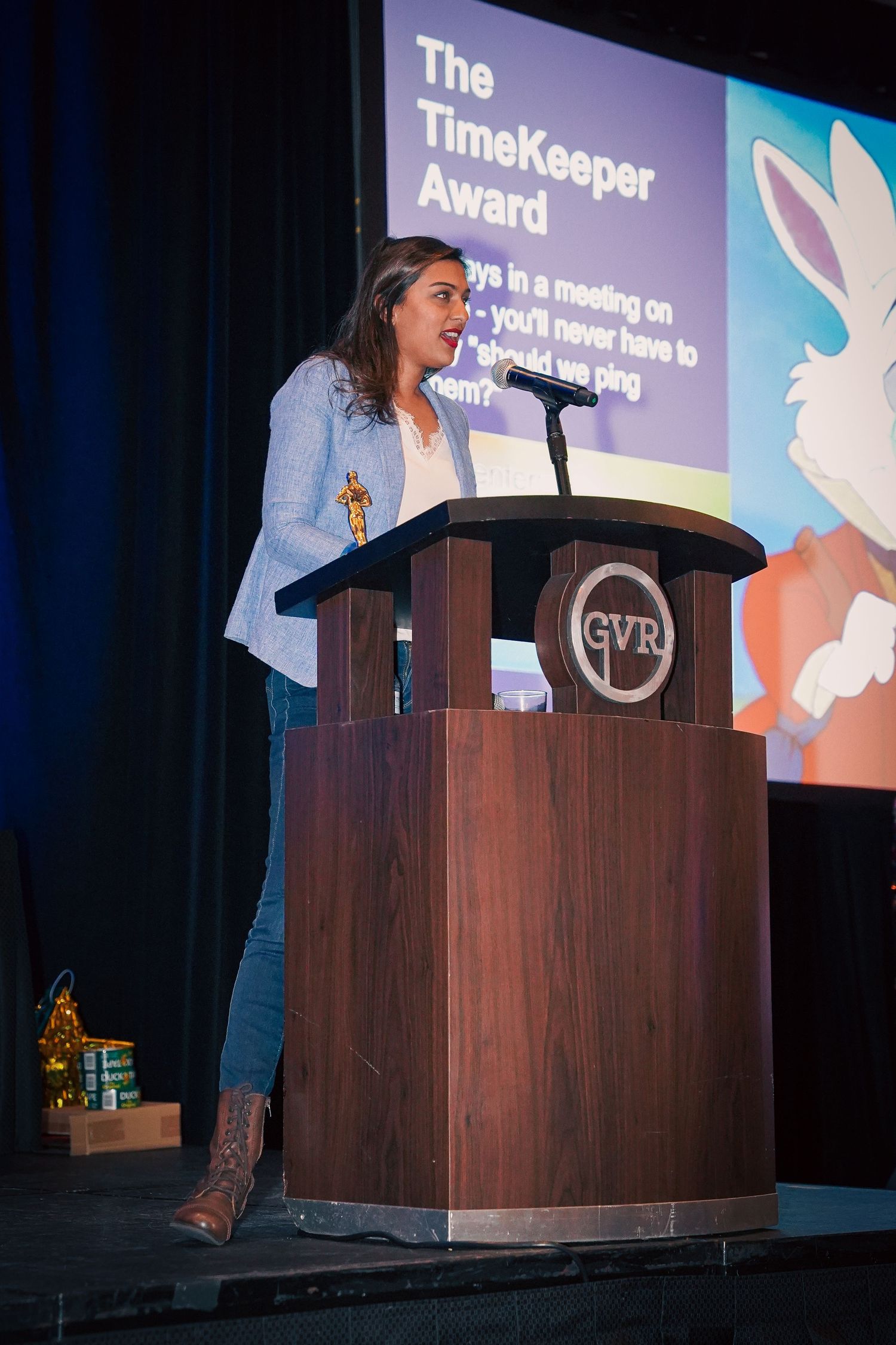 Speaker presents at podium with 'The TimeKeeper Award' displayed on screen during corporate ceremony.