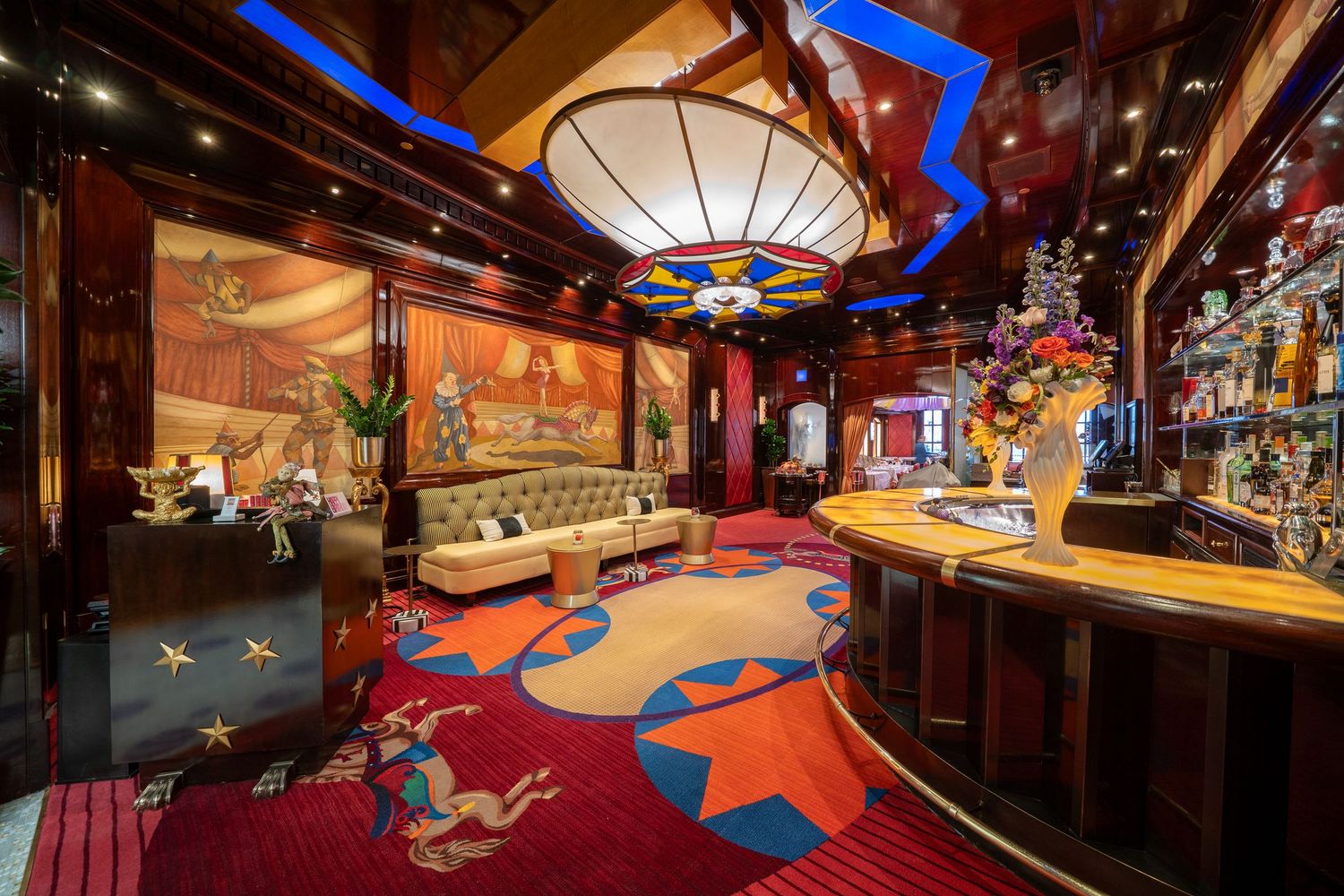 Modern bar lounge with Asian decor, curved seating, and dramatic lighting featuring a bold red and blue carpet design.