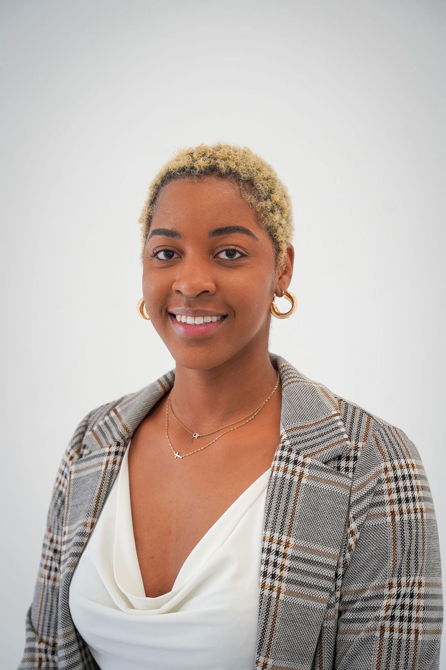 Monaco Media. Professional headshot of a woman wearing a plaid blazer and white top against a light background.