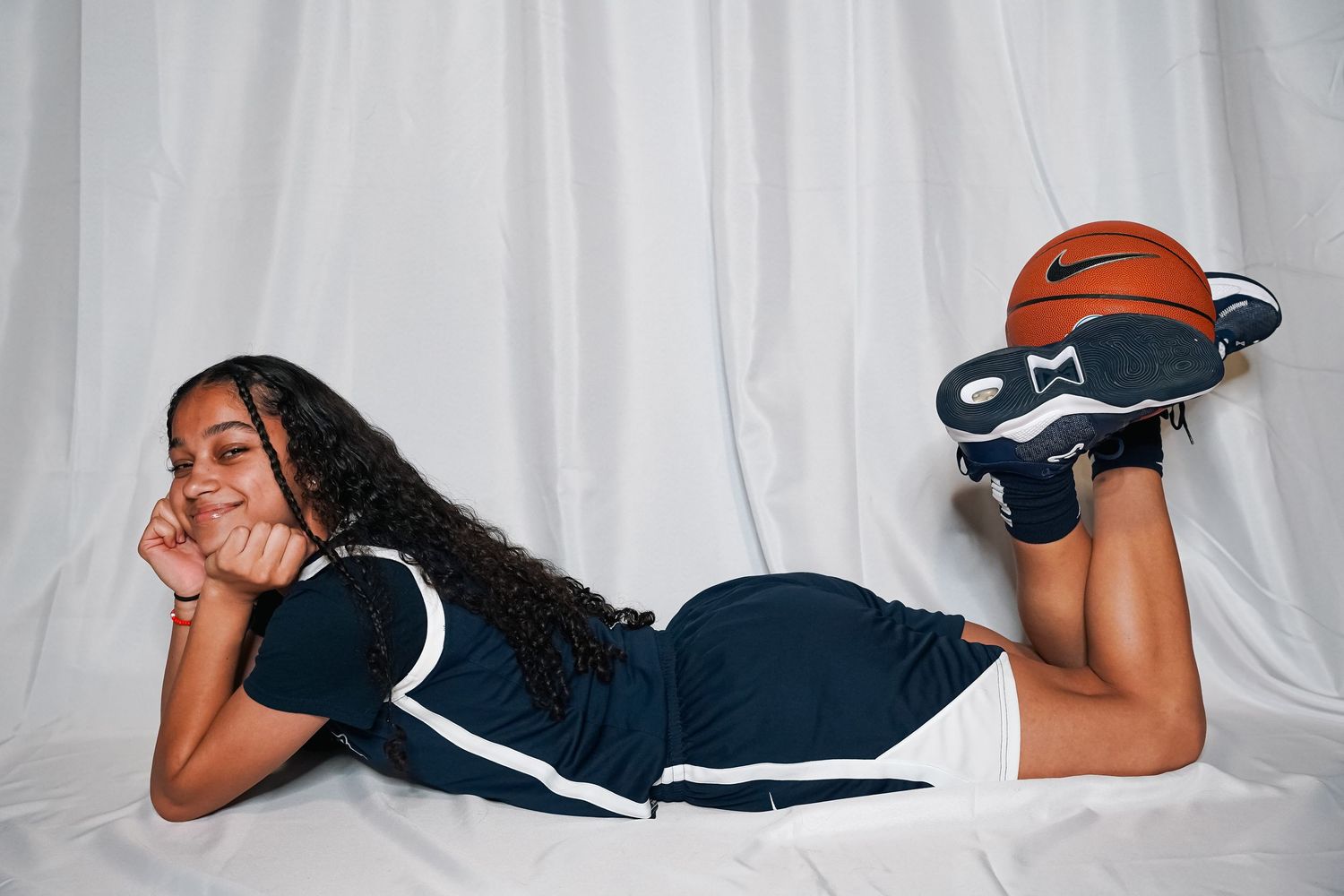 Basketball player in navy uniform poses laying down during photo session.