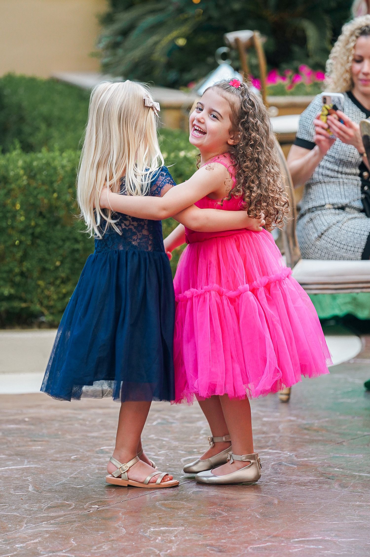 Two young girls in tulle dresses, one navy and one pink, dance together at an outdoor party.