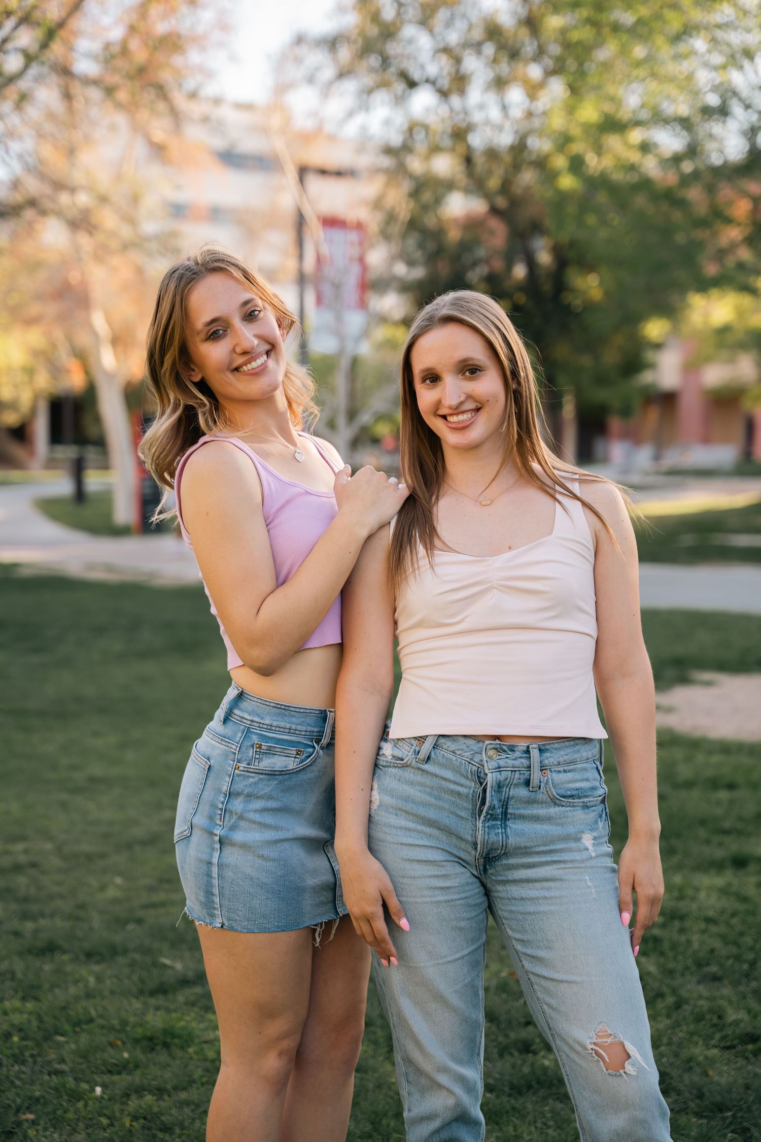 Friends in casual summer outfits pose together on a grassy campus lawn during golden hour.