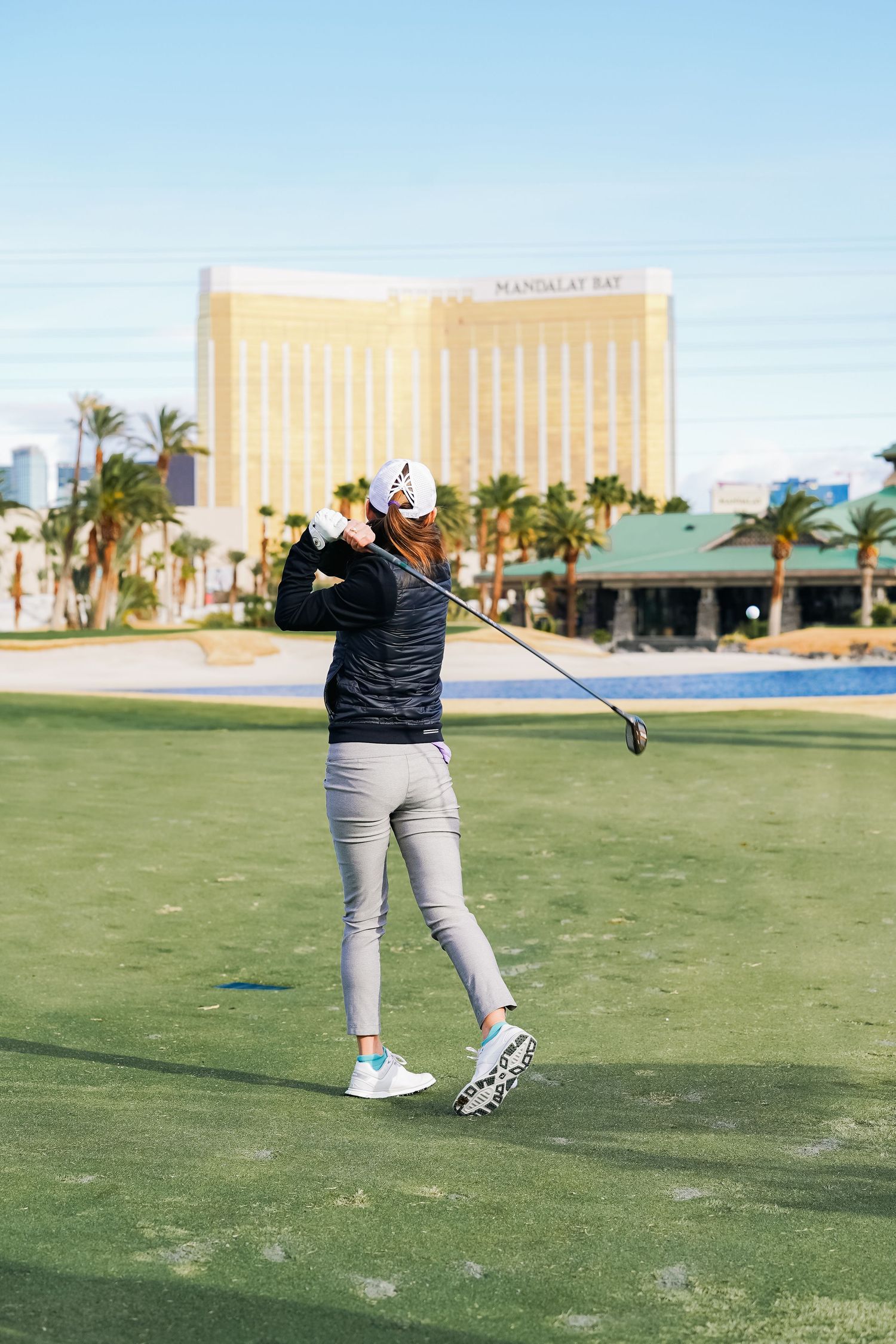 Golfer mid-swing on a golf course with a casino resort visible in the background.