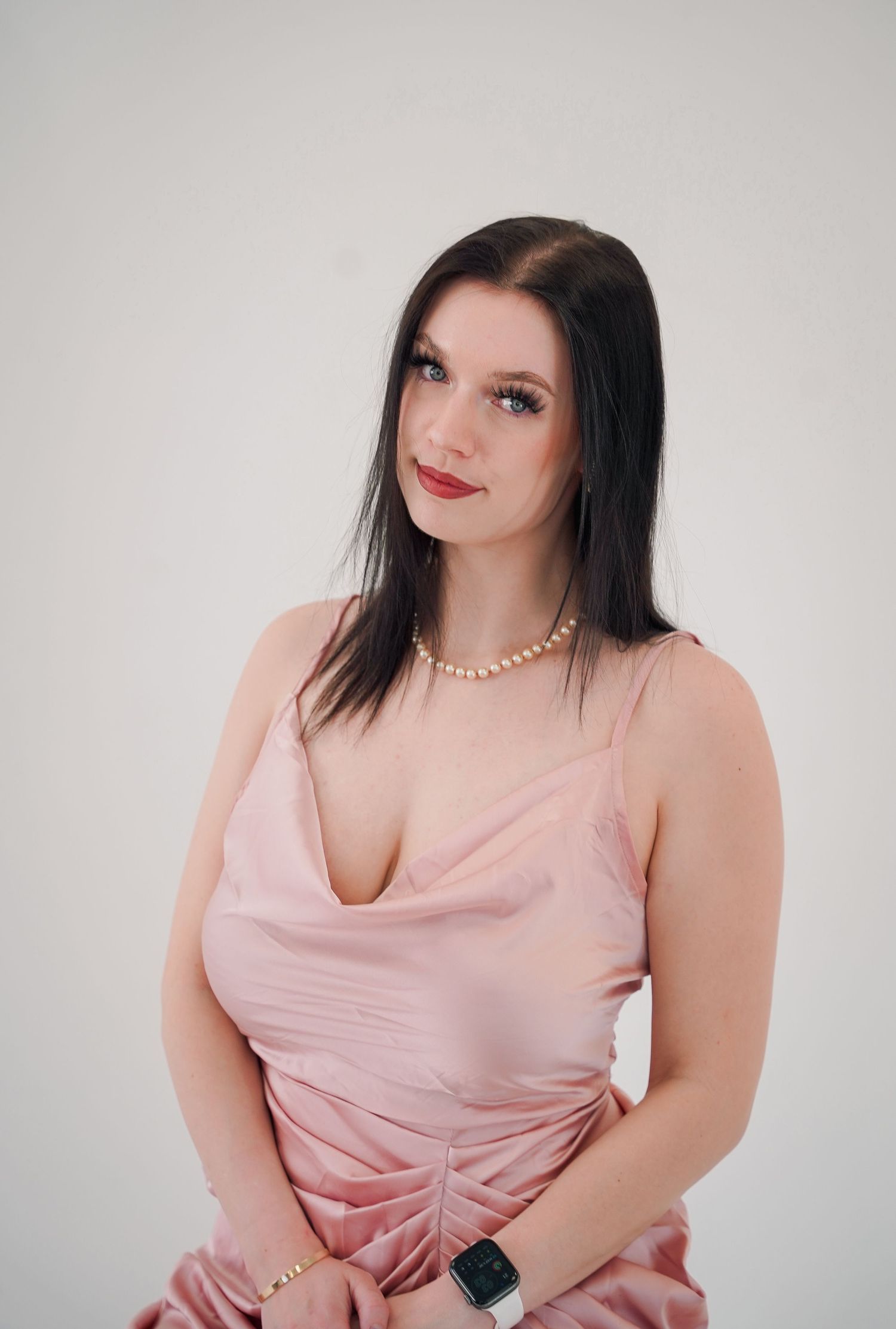 Woman in pink slip dress poses for portrait against white studio background.