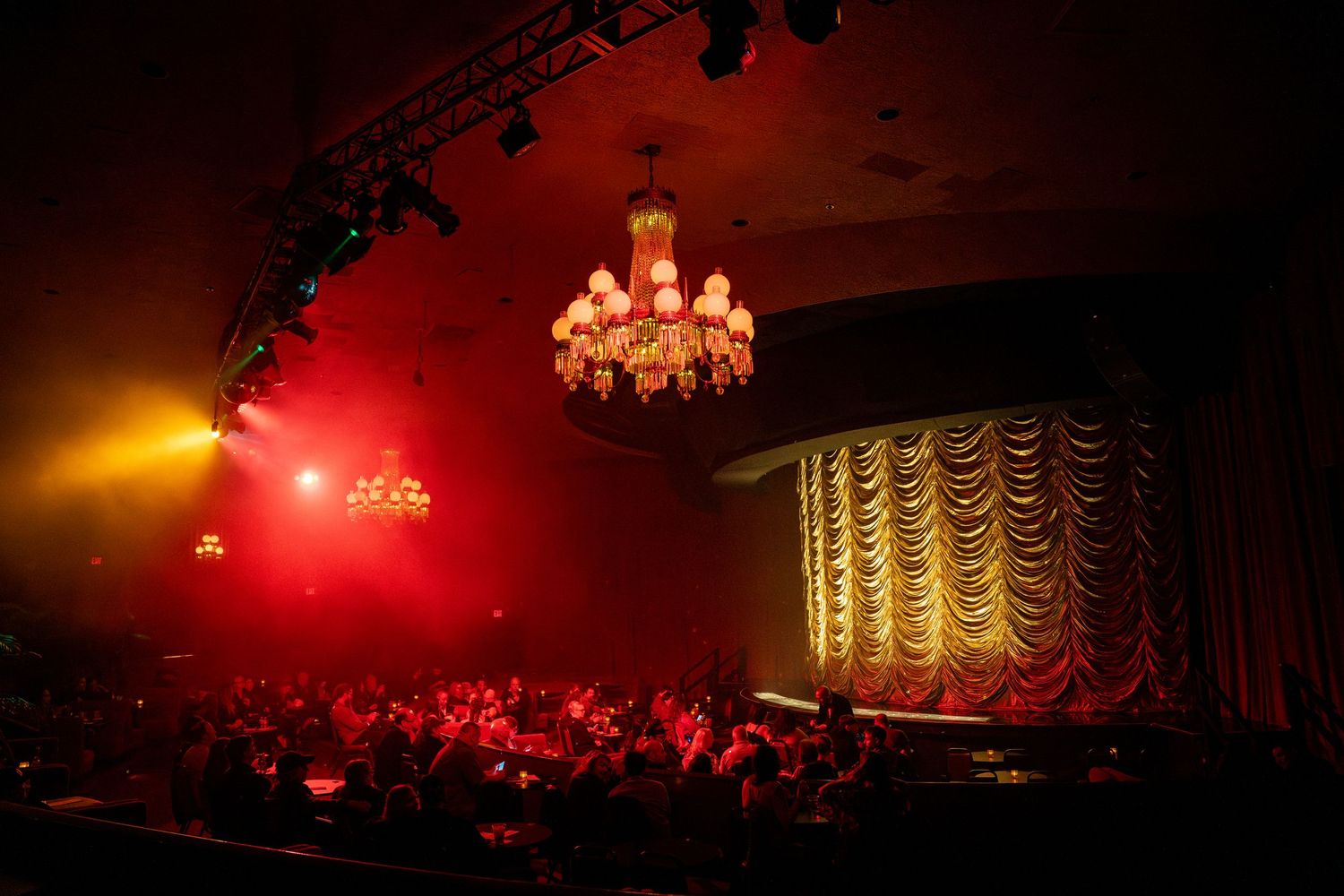 Elegant chandelier illuminating theater stage with gold draped curtains.