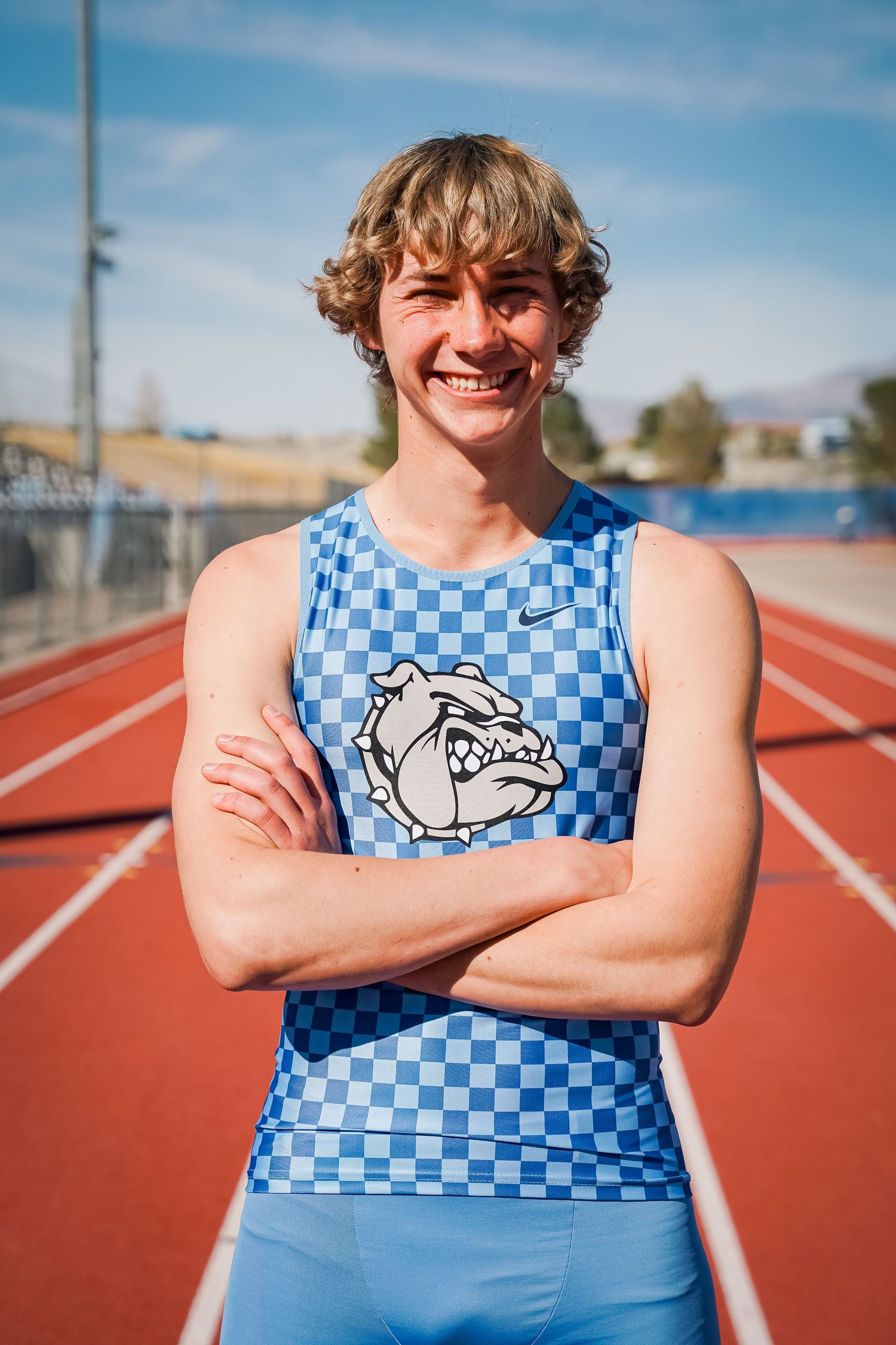 Track athlete wearing blue checkered Bulldogs uniform smiles confidently on outdoor running track.