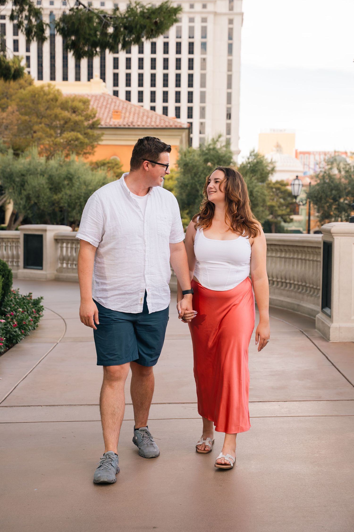 A couple enjoying an evening stroll along a walkway at a Las Vegas resort with hotel buildings in the background.
