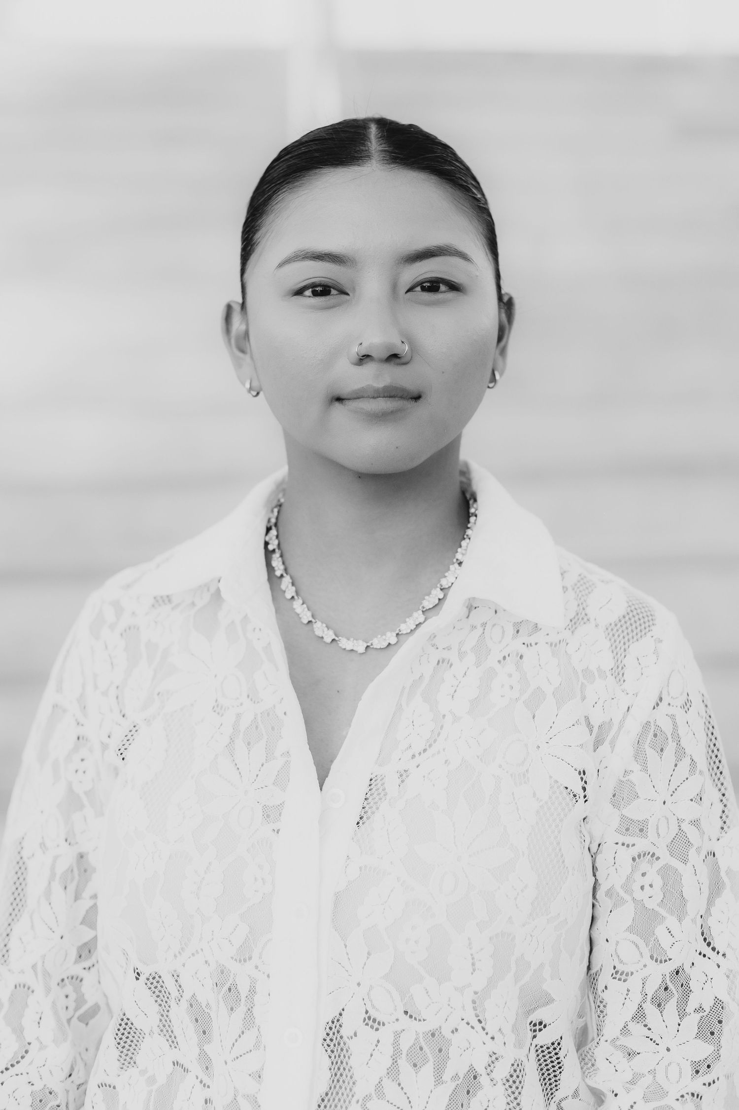 JJ Monaco. Black and white professional portrait with lace blouse and statement necklace against neutral background.