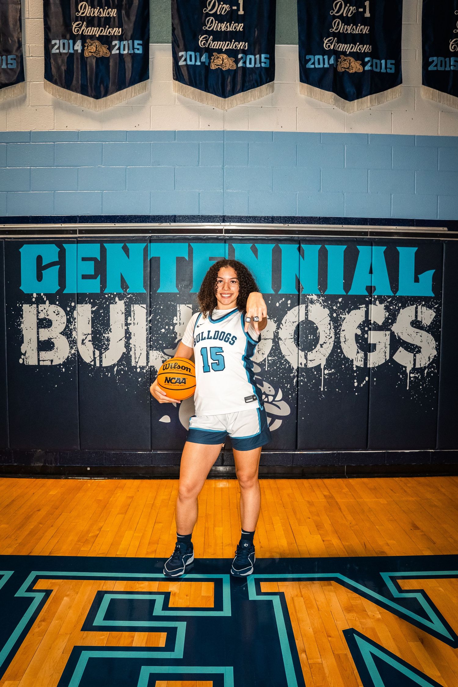 Player in white and blue uniform posing with basketball on wooden court floor.