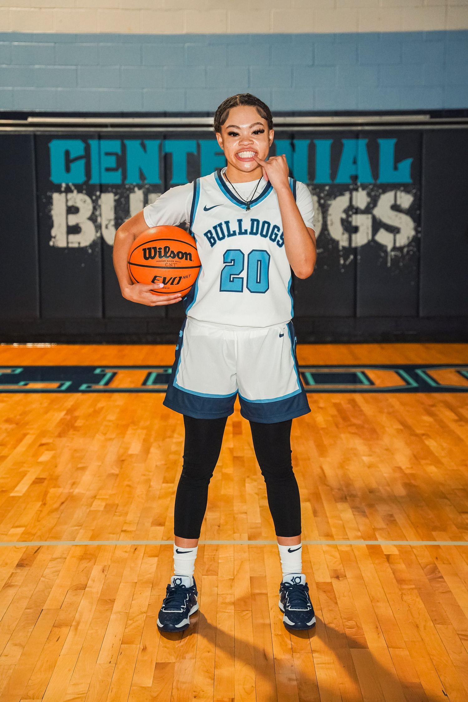 Basketball player in white Bulldogs jersey number 20 poses with ball in front of team logo.
