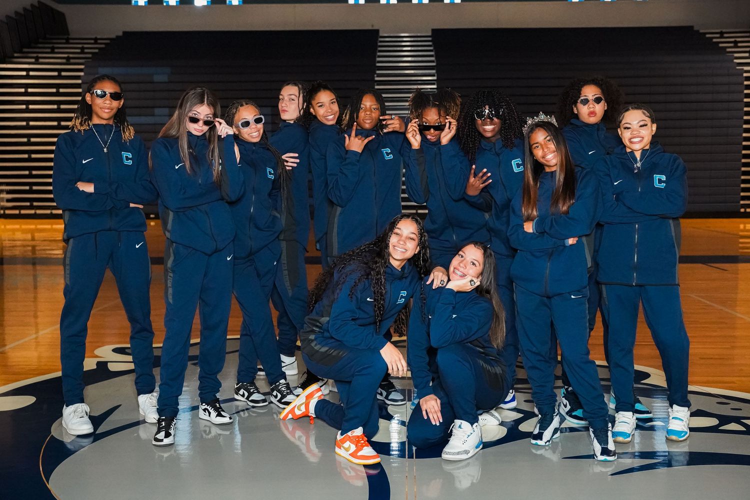 Group photo of basketball team members in navy warm-up uniforms posing casually in gym.