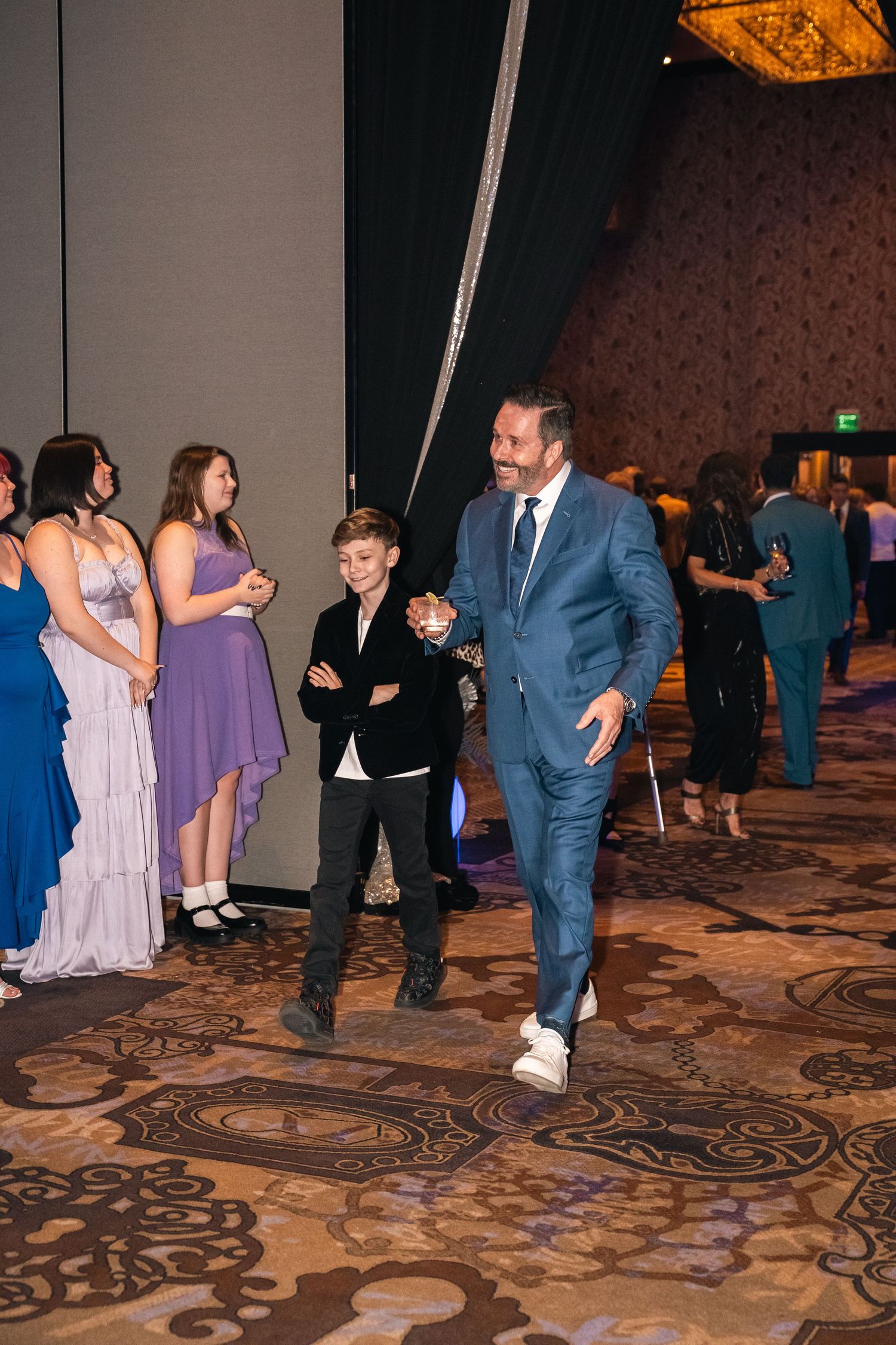 People in formal attire socializing at an elegant event with patterned carpet.