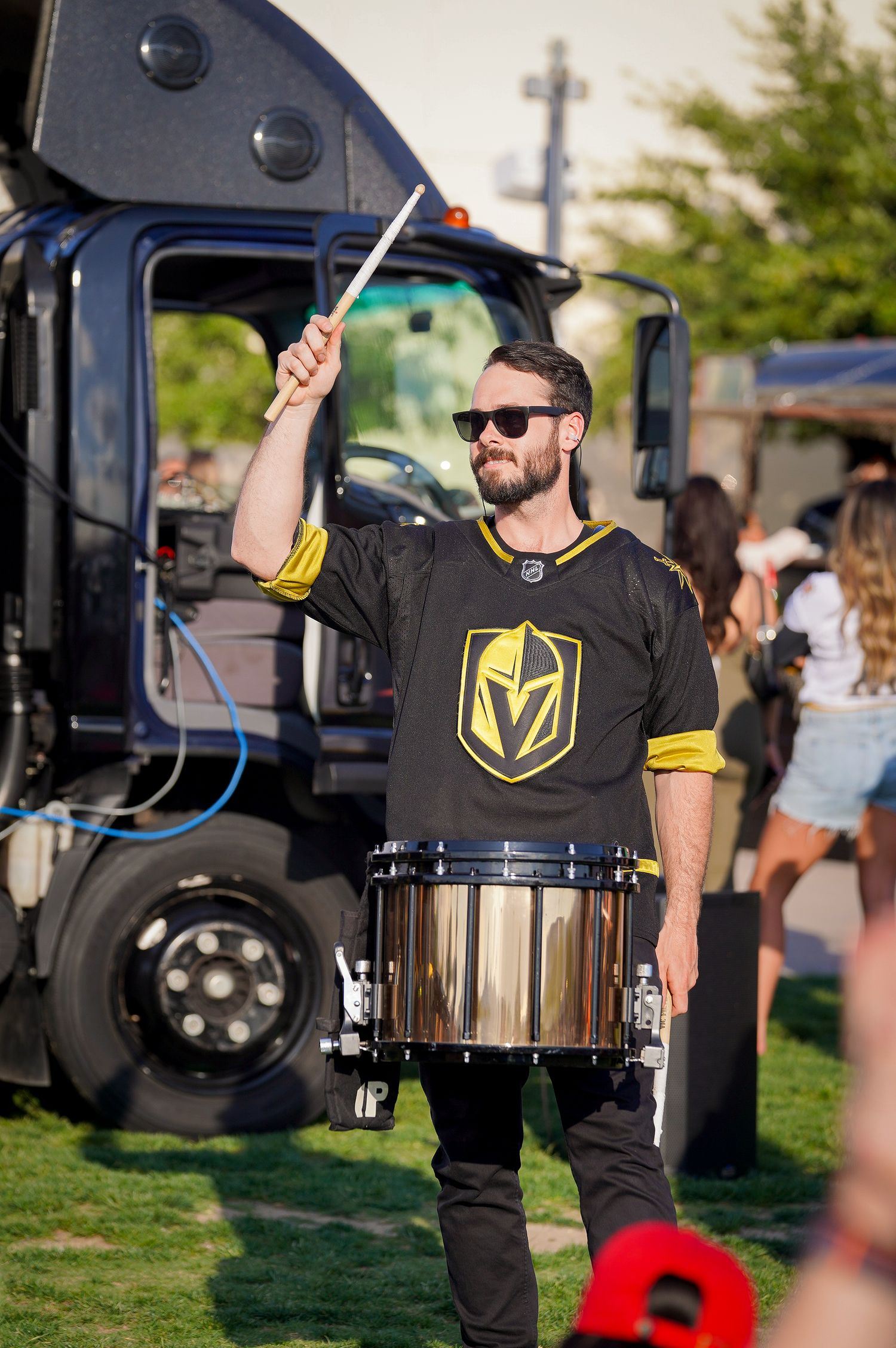 Drummer in Vegas Golden Knights jersey performs with drumsticks at an outdoor event.