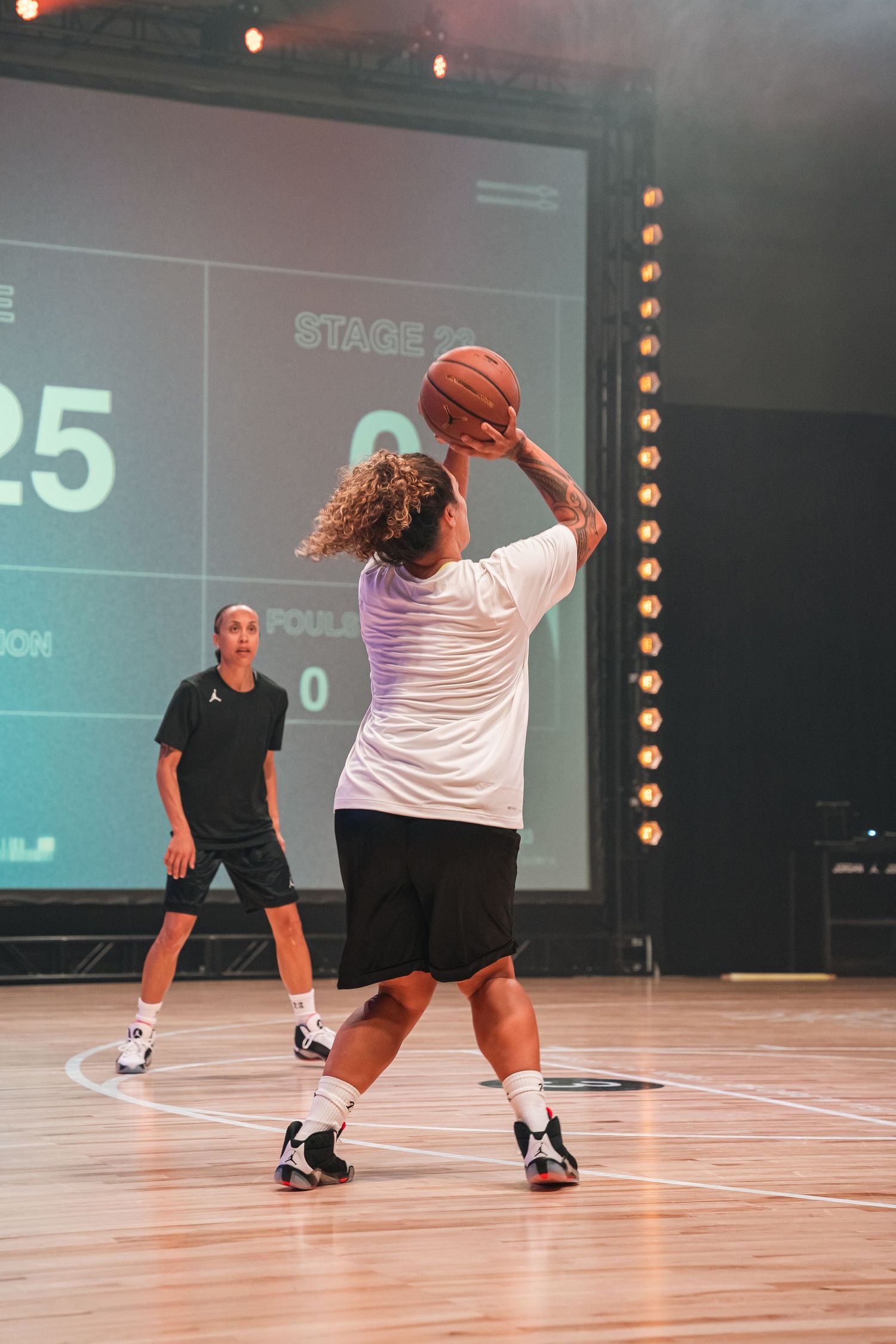 Basketball player shooting the ball with scoreboard visible in background.