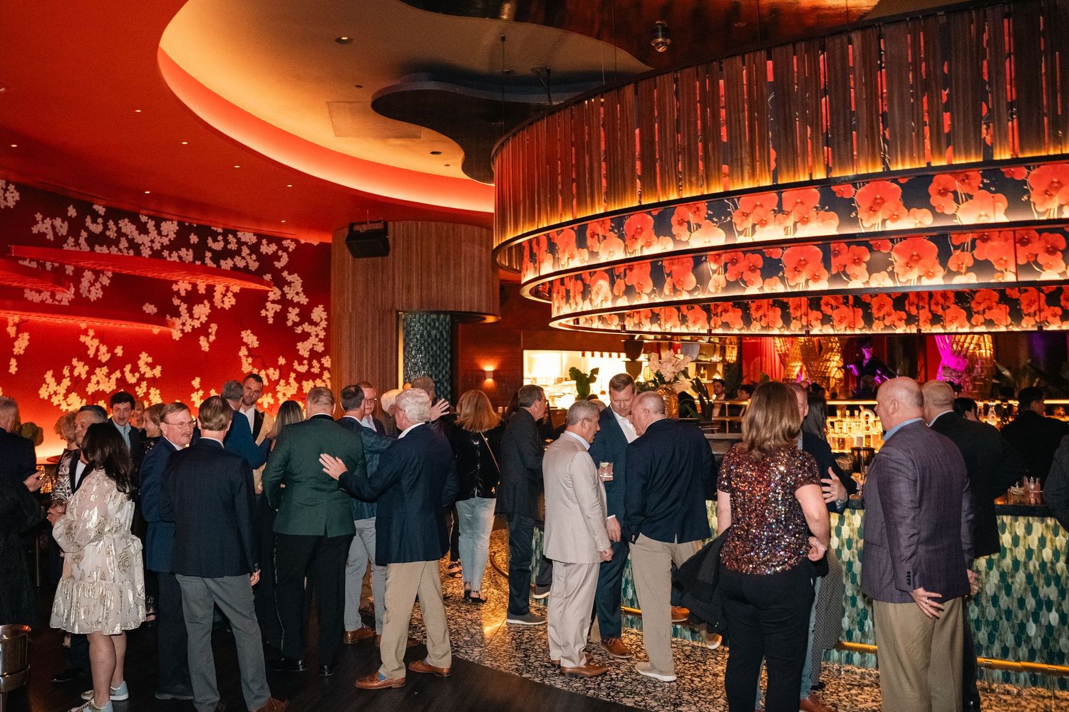 Elegant bar with red lighting and decorative elements filled with patrons enjoying a social gathering.