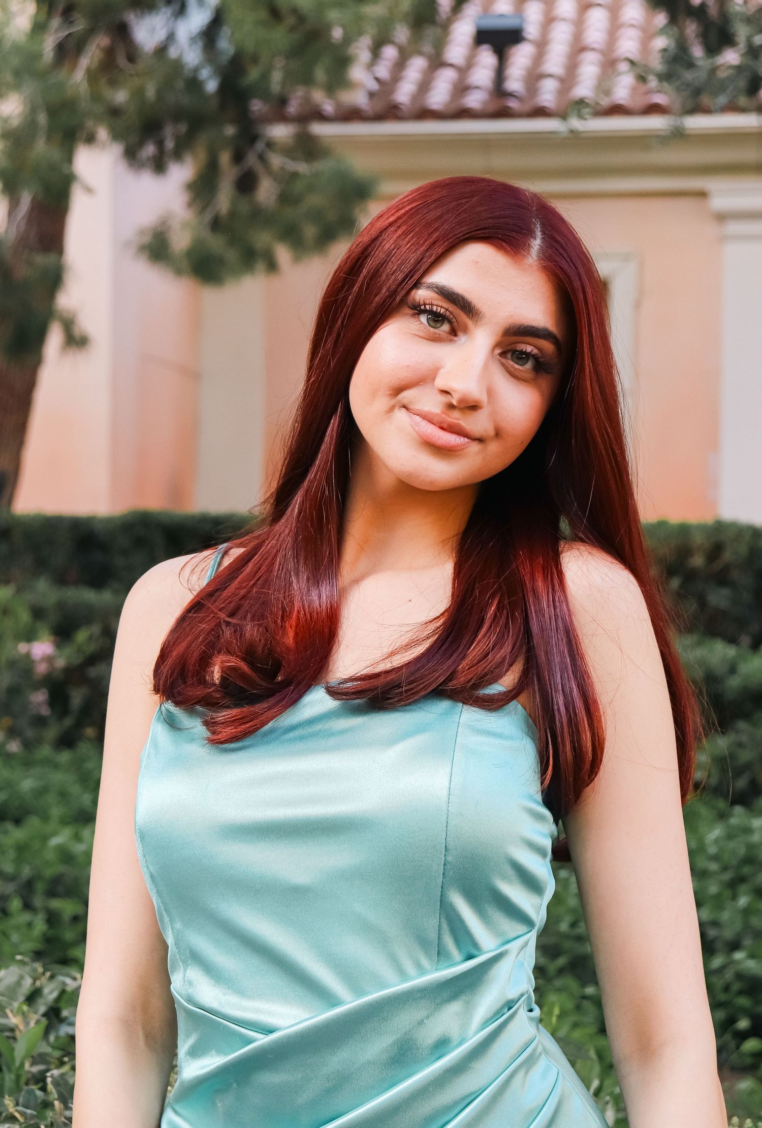 Woman in mint satin dress poses outdoors against pink stucco building background.