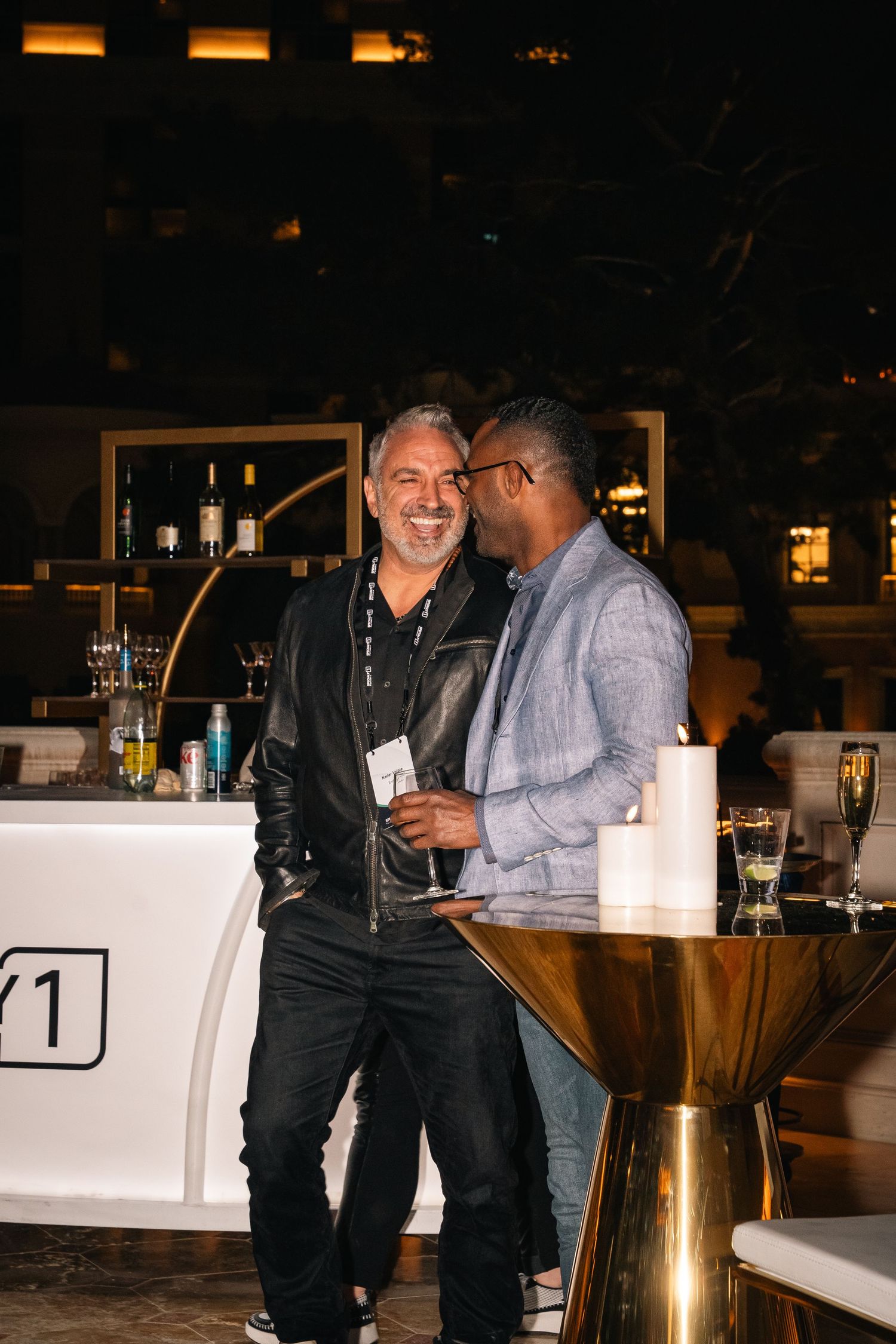 Two professionals sharing conversation at an evening networking event near a bar setup.