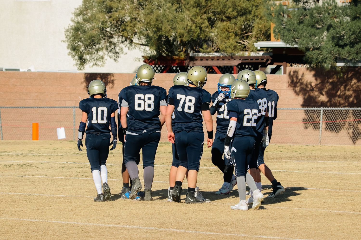 Football teammates in navy uniforms walking together on field during practice.