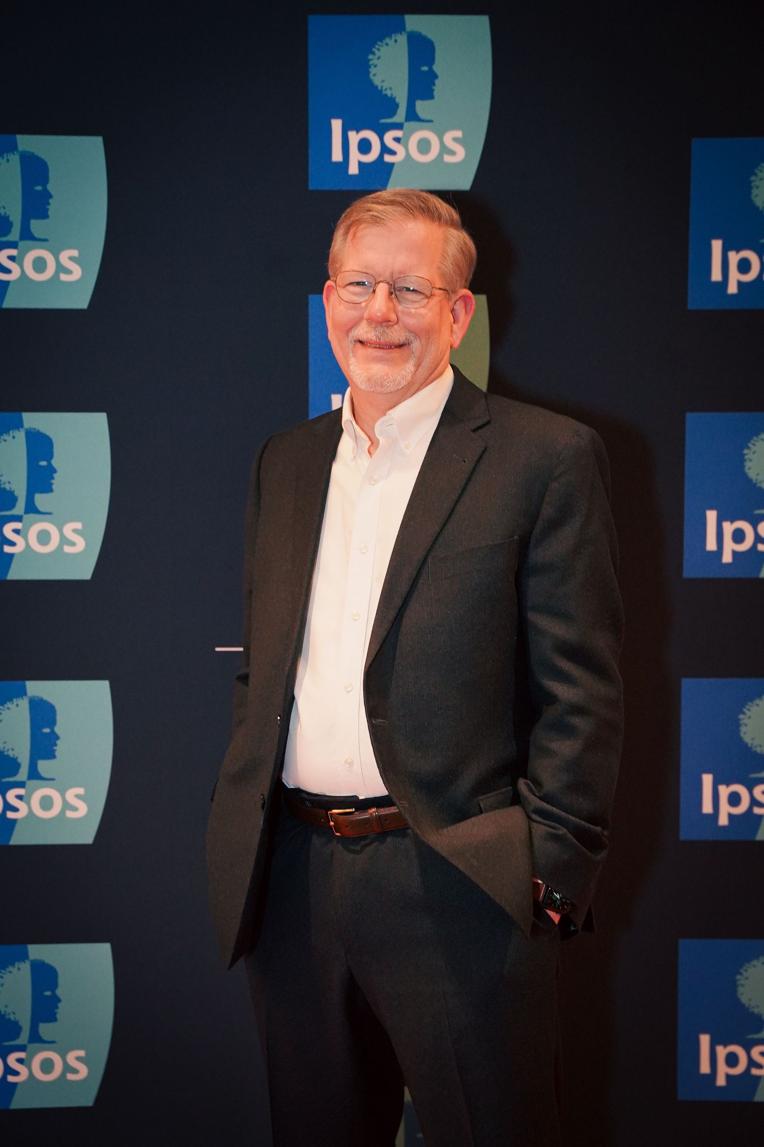 Professional headshot against an Ipsos branded backdrop with dramatic lighting.