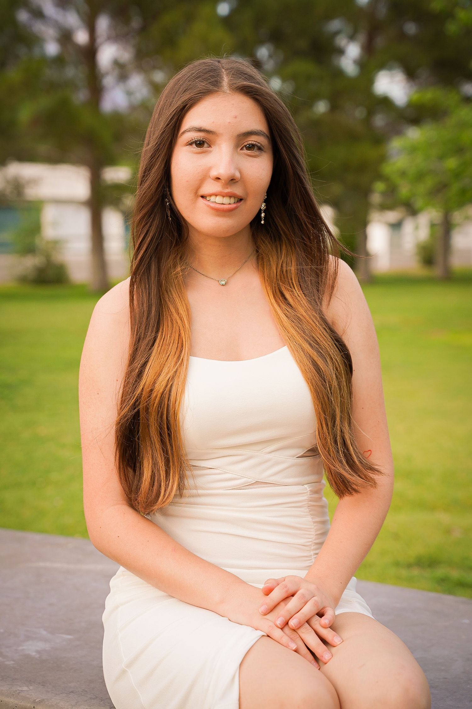 Graduate poses in white dress for portrait on campus grounds.