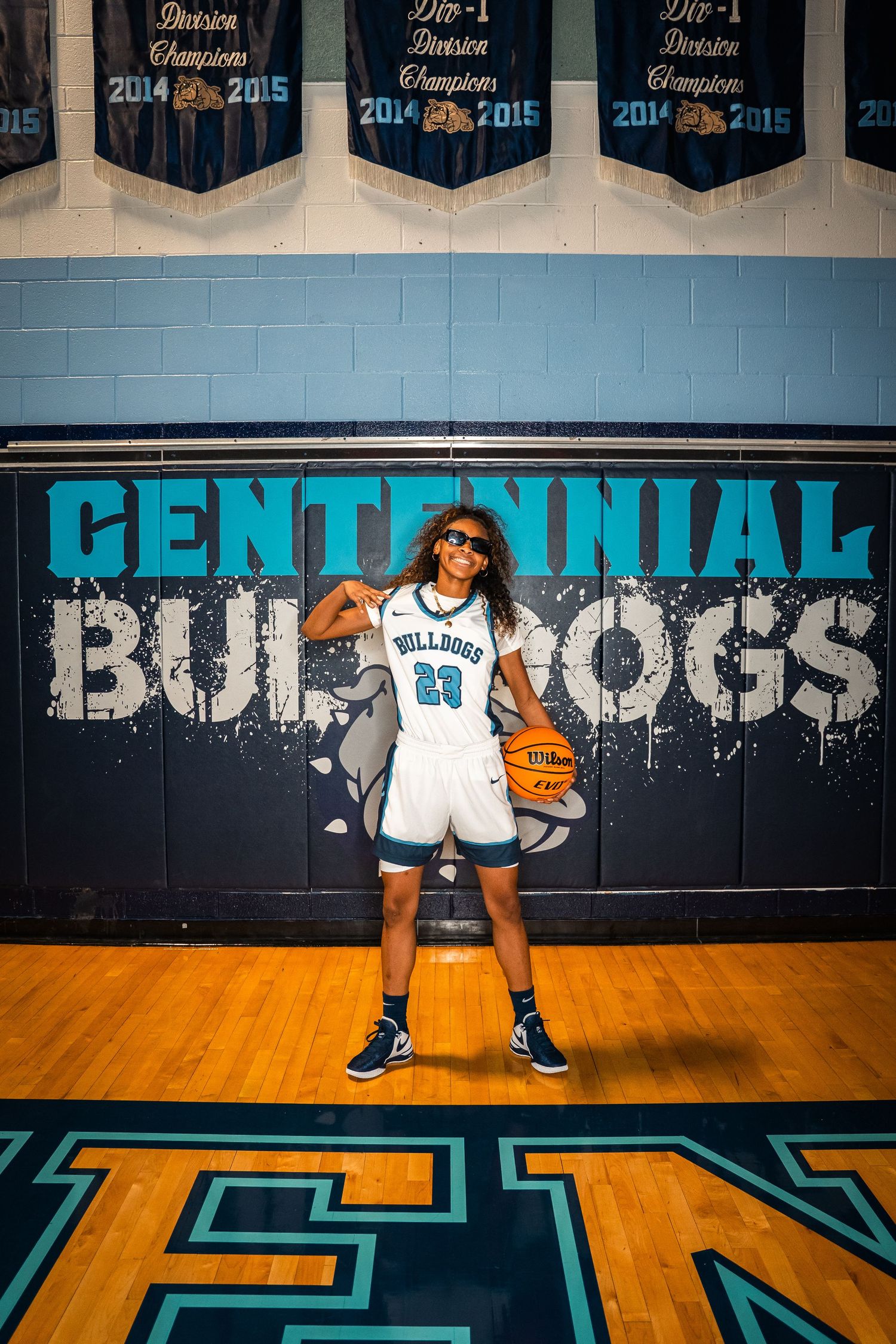 Basketball player posing in defensive stance with basketball on hardwood court.