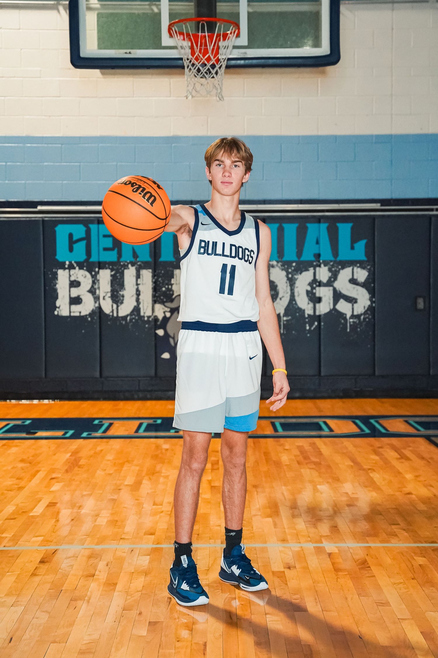 Basketball player in white Bulldogs uniform posing with ball in gym.