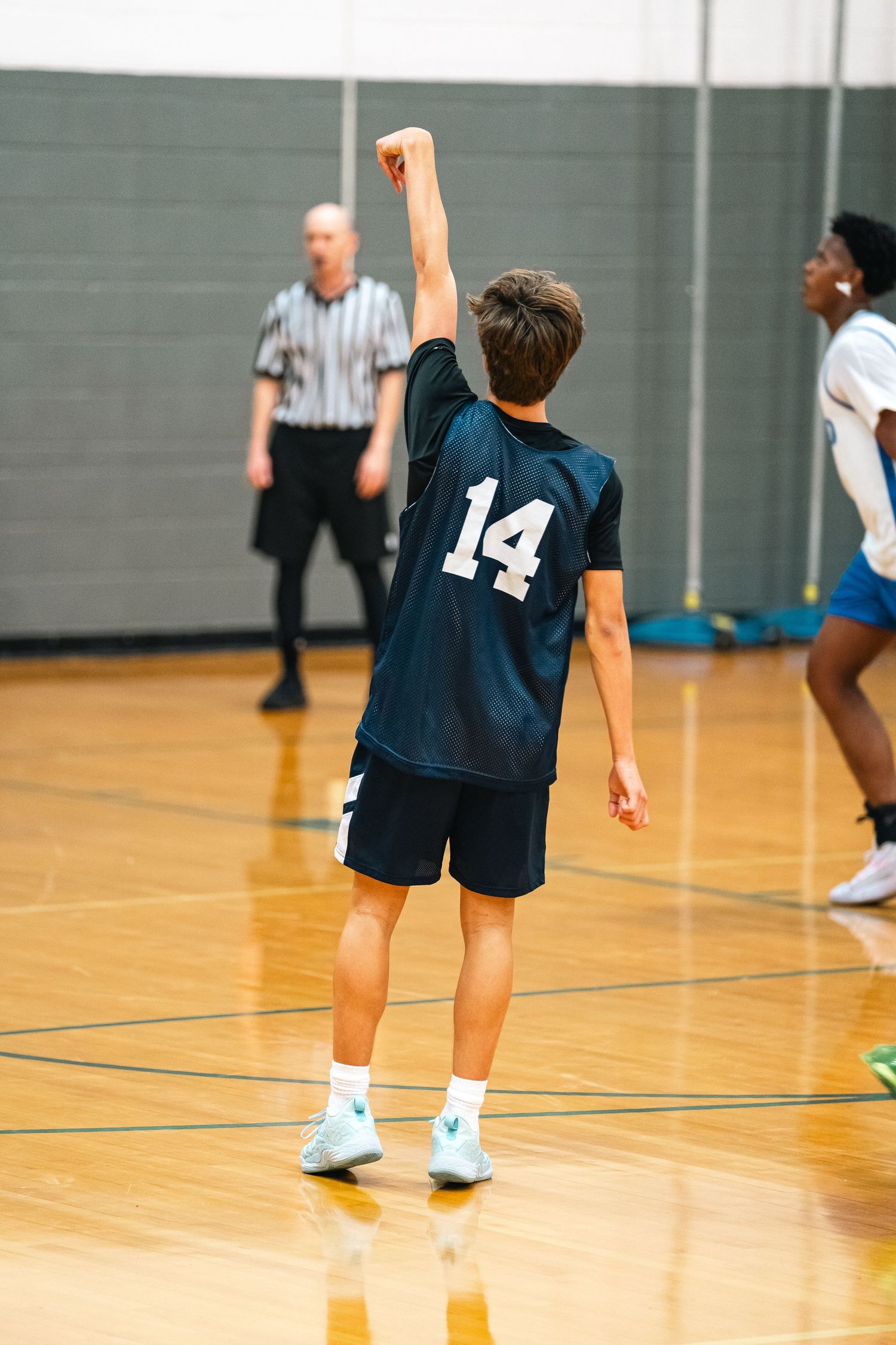 Young basketball player in navy jersey holds follow through after shooting the ball.