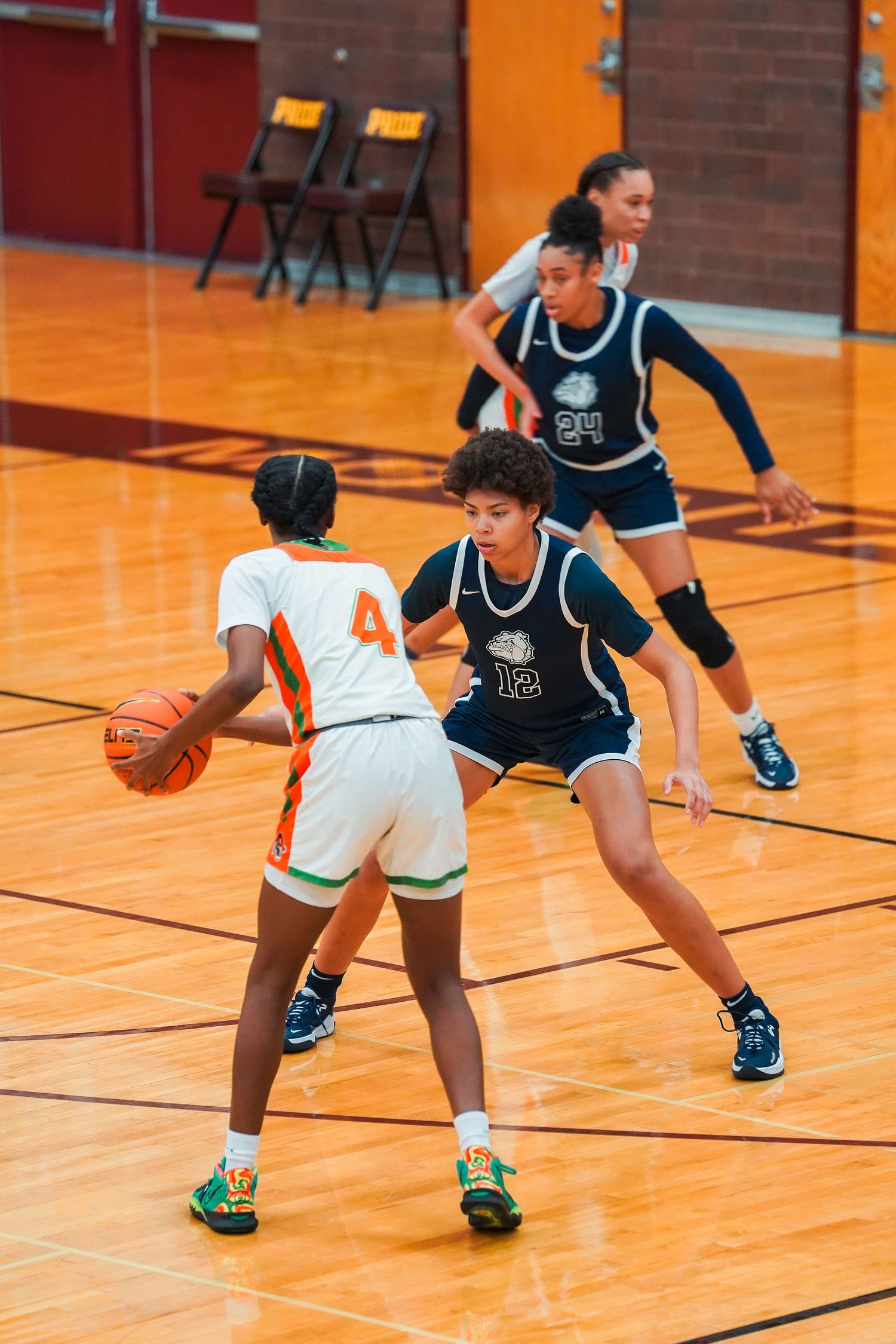 Basketball players in navy and white jerseys compete in defensive positions on a gymnasium floor.