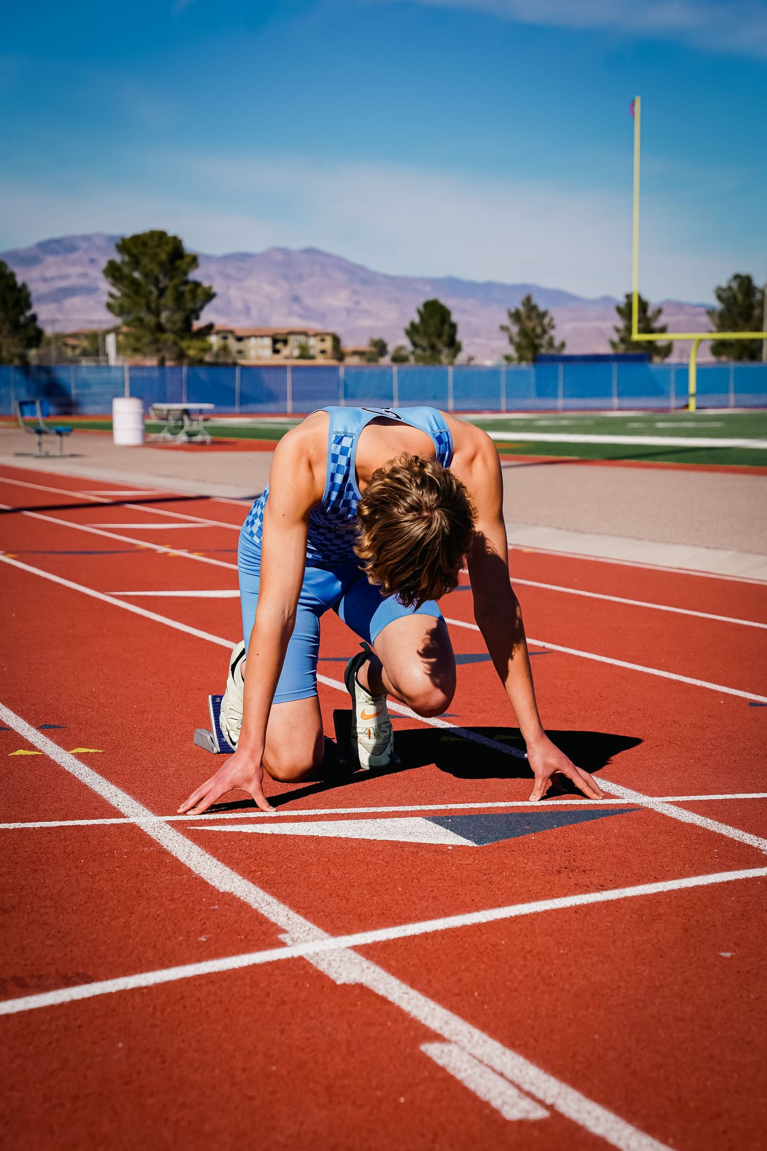 Athlete in starting position on red track under blue sky.