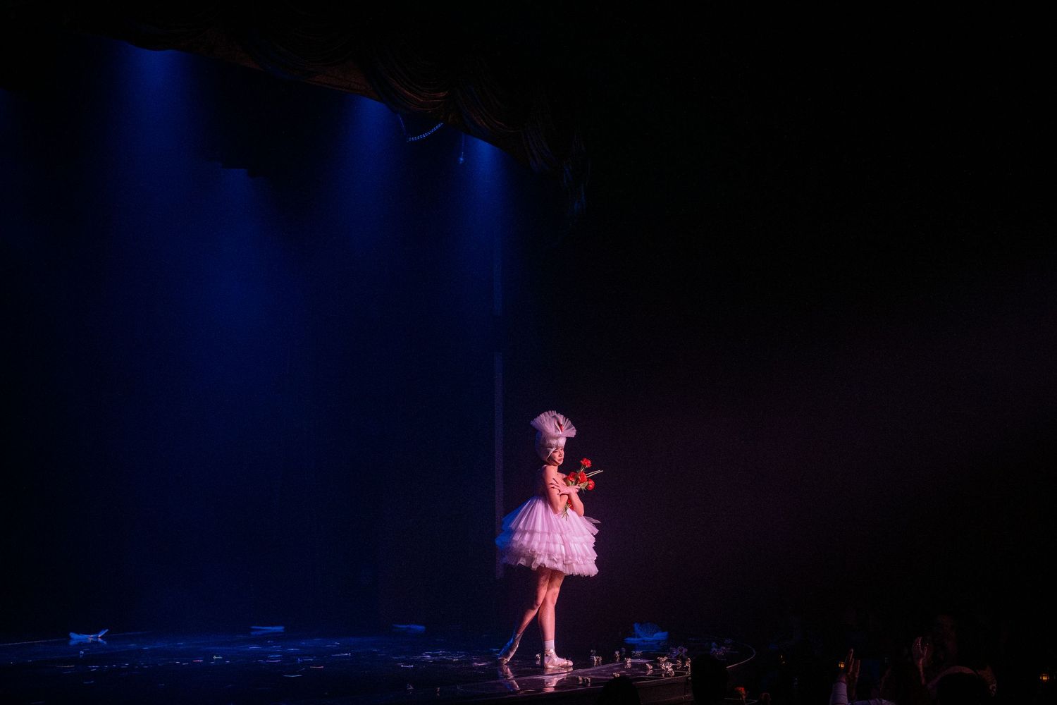 Stage performer in pink costume under dramatic blue spotlight.