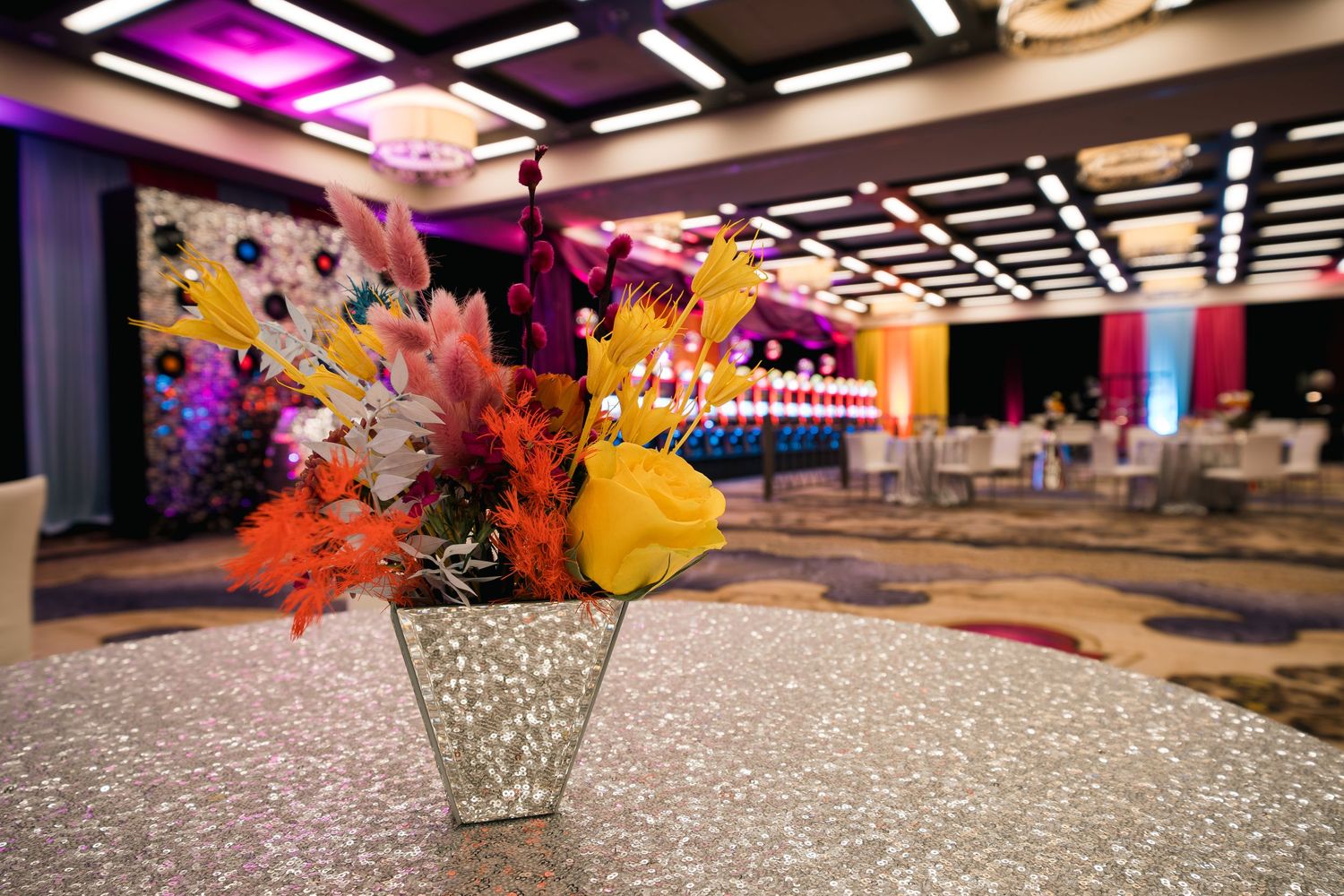 Colorful floral centerpiece on glitter tablecloth with casino ballroom in background.