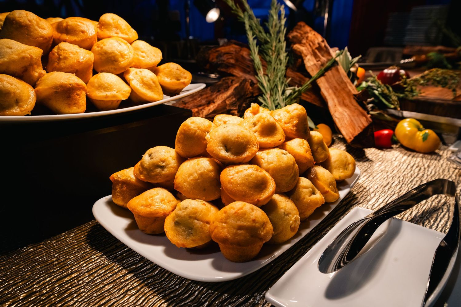 Fresh baked golden dinner rolls piled high on white serving platters with herbs and garnishes.