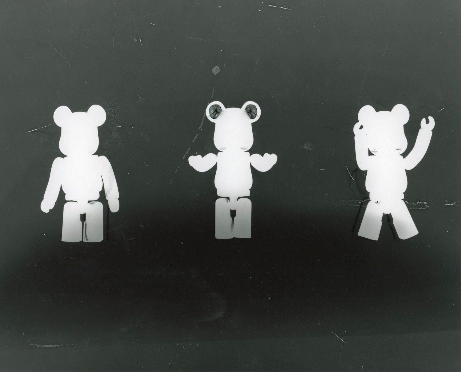 Negative image of three toy bear figures in white against black background.
