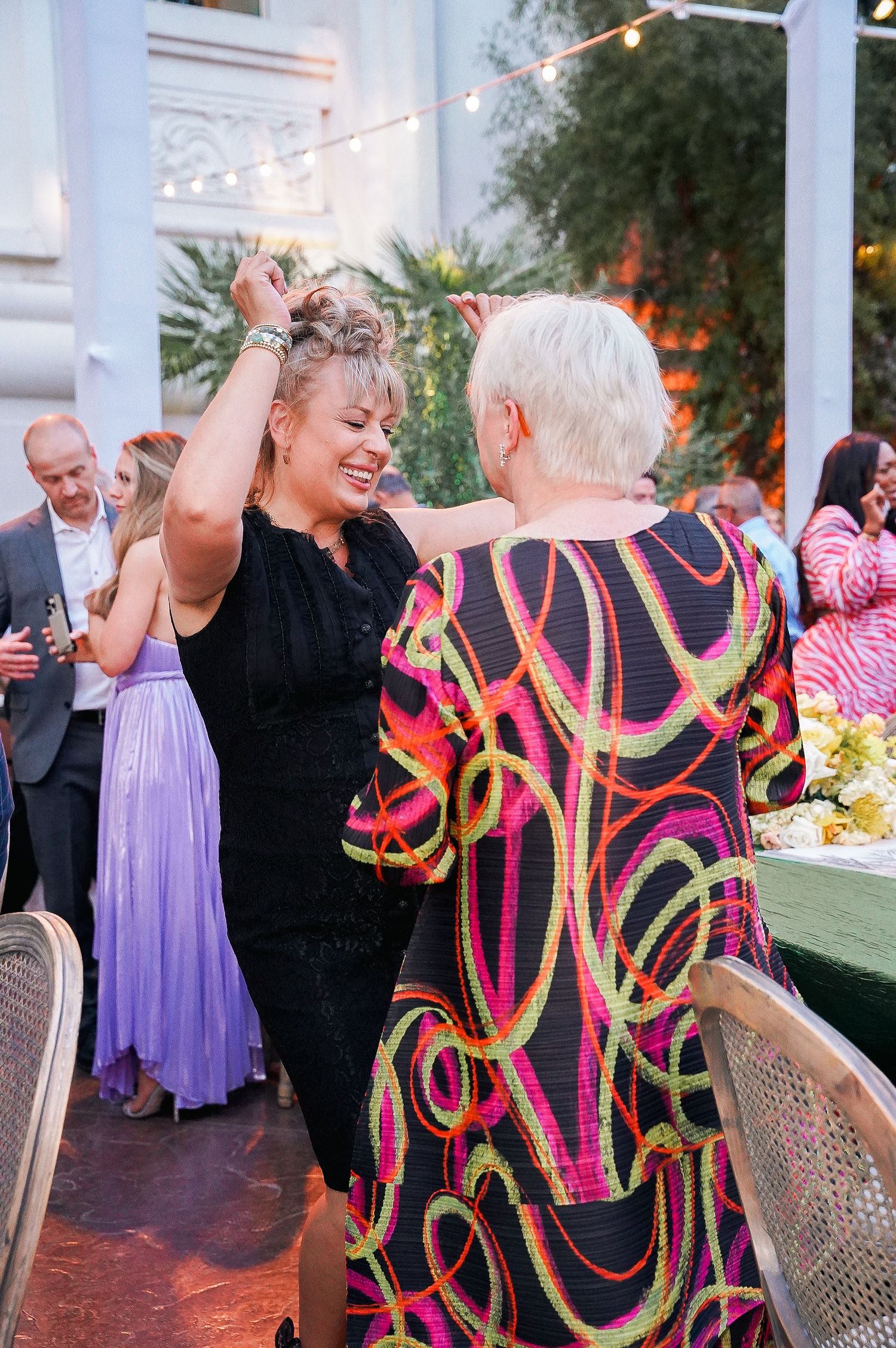 Two guests dancing energetically at an outdoor celebration with string lights and decorative details.