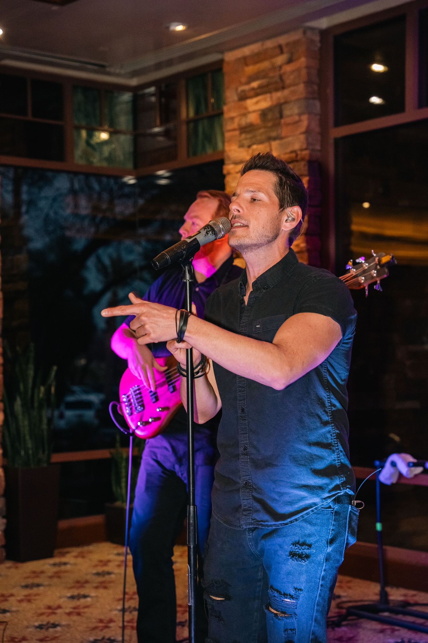 Singer performing with a microphone in a dimly lit venue with stone walls and mood lighting.