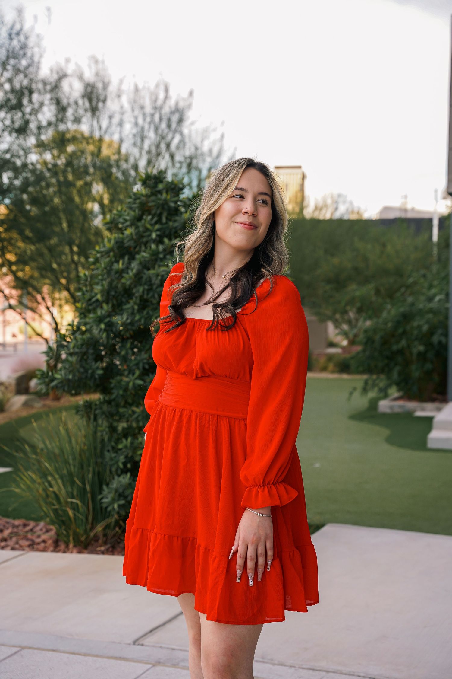 Graduate in flowing red dress poses outdoors during graduation photoshoot.
