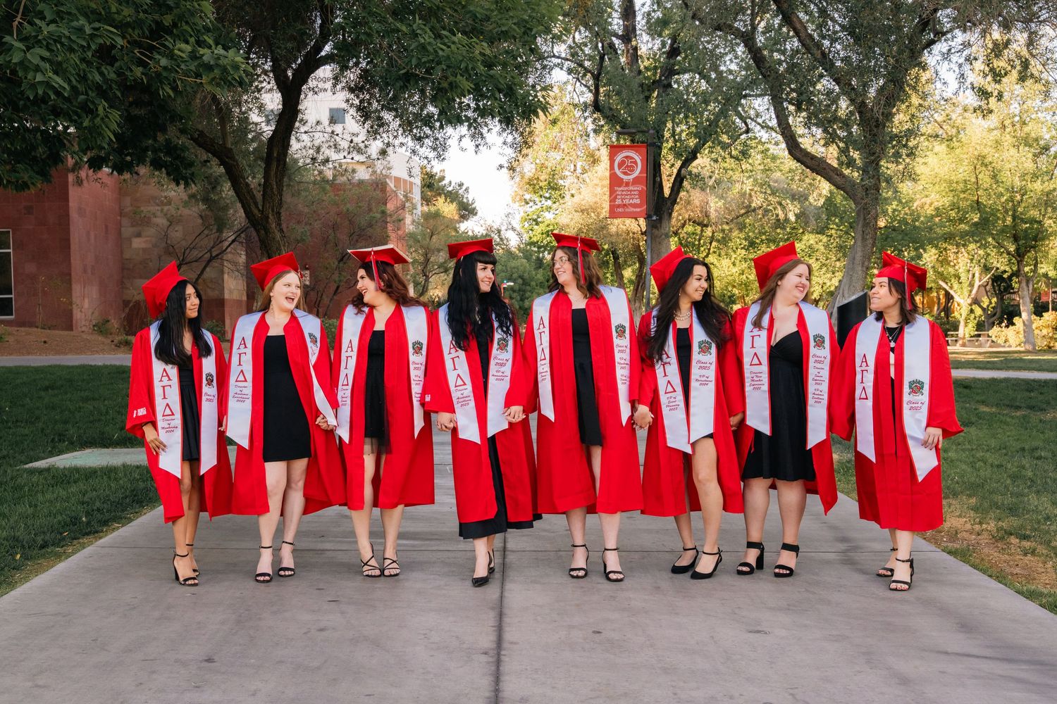 Graduates in red caps and gowns pose together on campus sidewalk with traditional graduation attire.