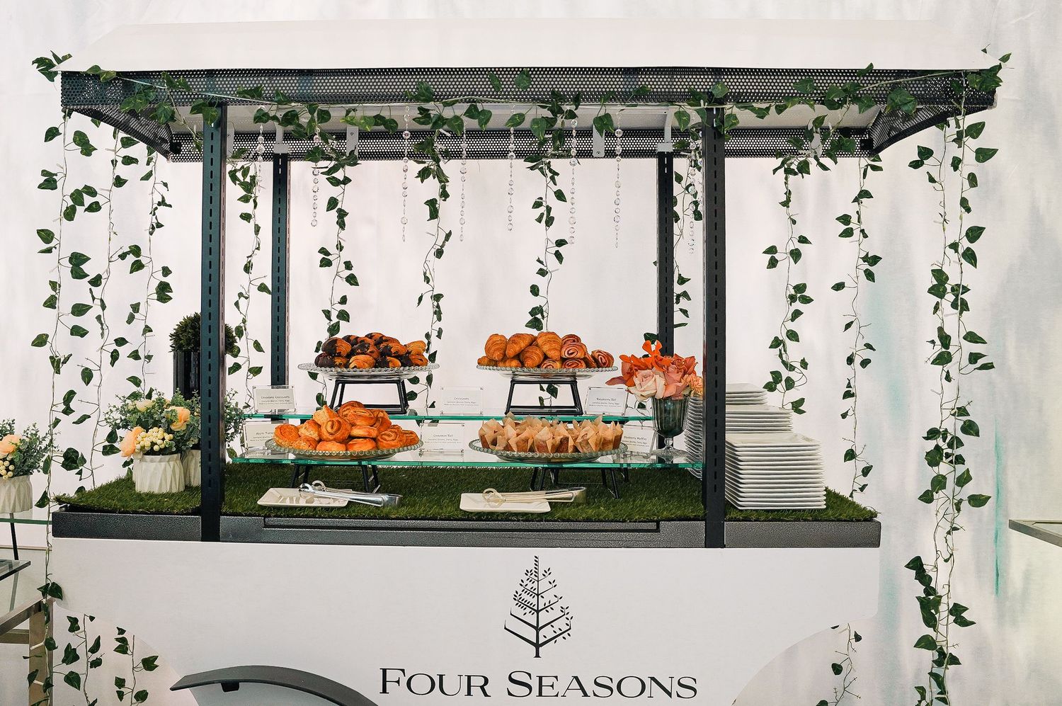 Four Seasons display with orange cakes under a pergola decorated with hanging greenery.